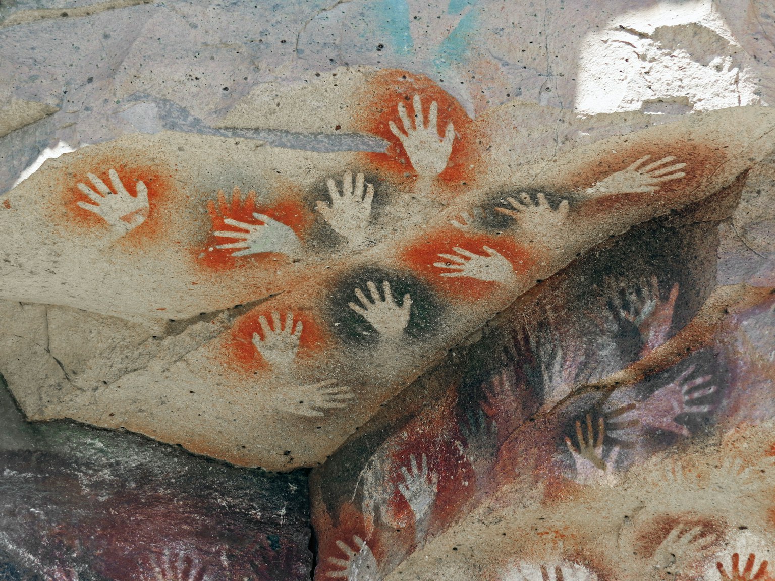 ภาพนี้แสดงรอยมือโบราณบนผนังถ้ำ รอยมือสีแดงและขาวซ้อนกันสร้างงานศิลปะทางประวัติศาสตร์