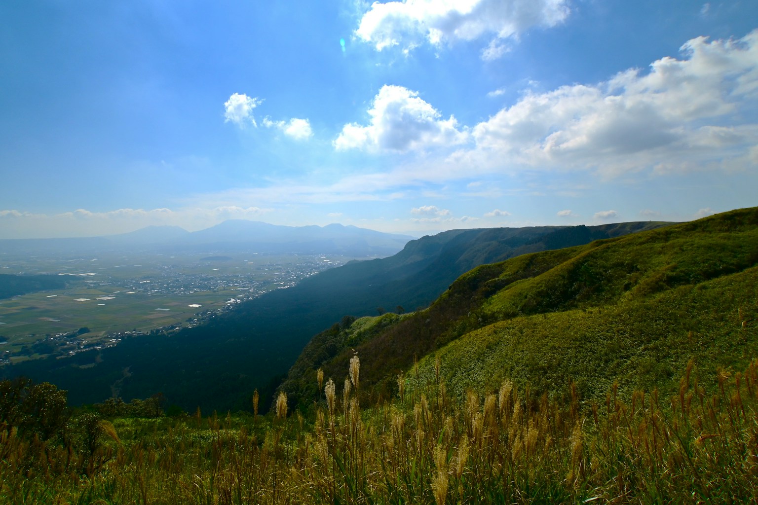 Vista panoramica di colline verdi sotto un cielo blu con nuvole montagne in lontananza
