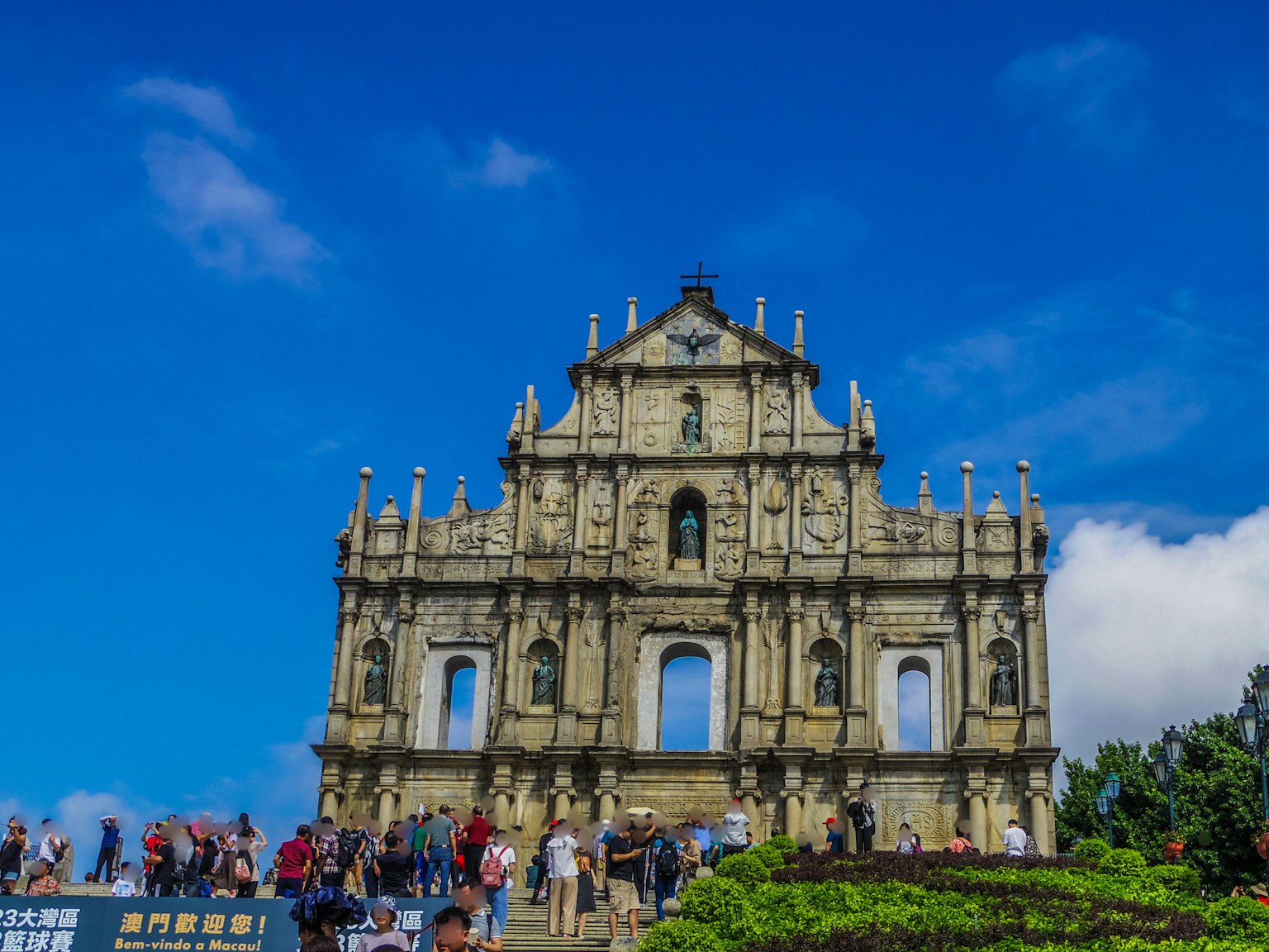 Fassade der Ruinen von St. Paul in Macau mit Touristen unter einem blauen Himmel