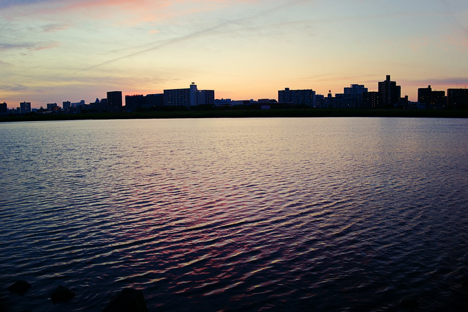 Silhouette d'une ville au coucher du soleil se reflétant sur l'eau