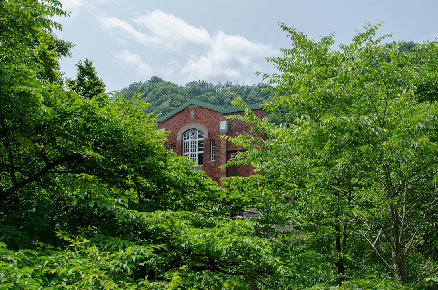 Red brick building surrounded by lush green trees and blue sky