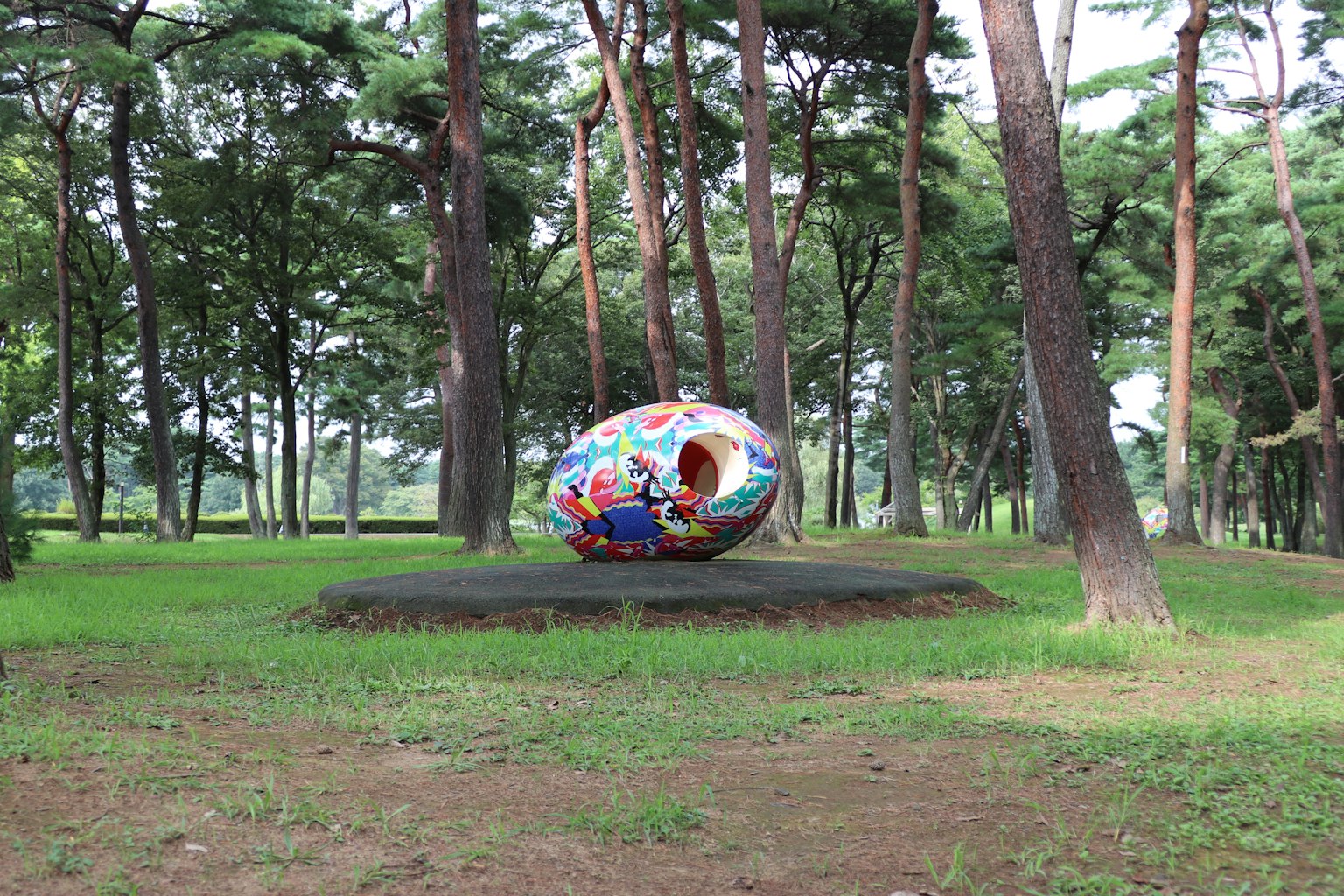 Patung berwarna-warni yang dikelilingi pepohonan di taman hijau