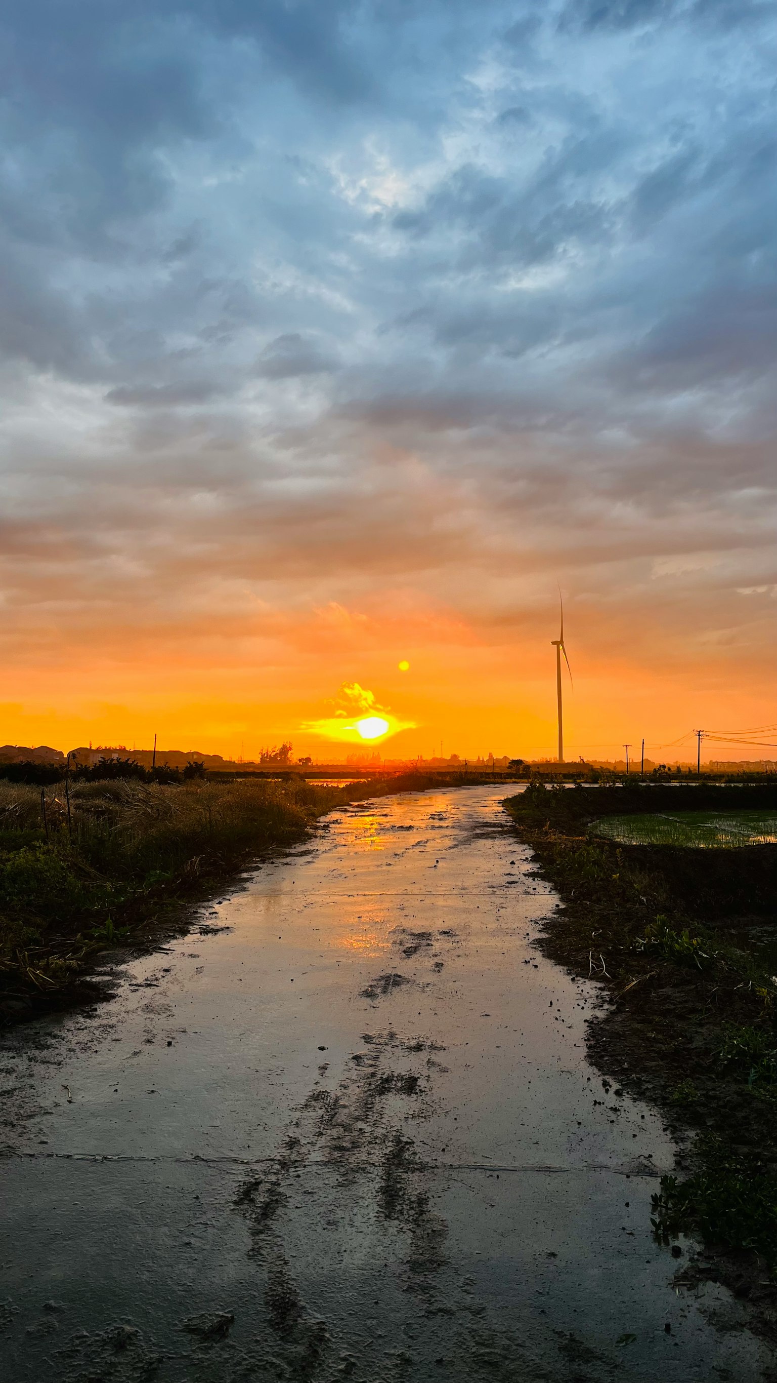 Paisaje de un camino al atardecer con nubes y reflejos en charcos