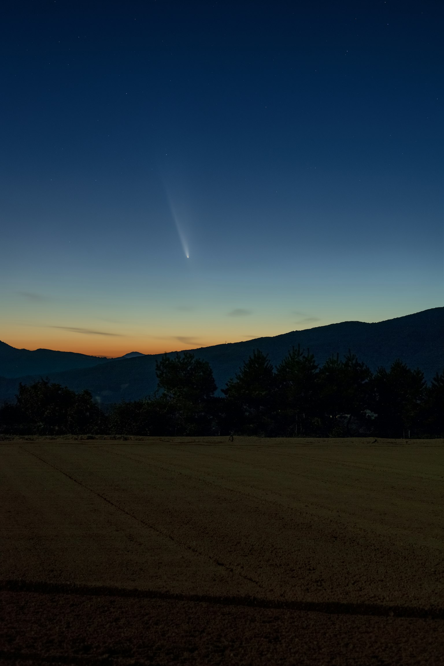 Cometa che appare nel cielo al crepuscolo con silhouette di montagne