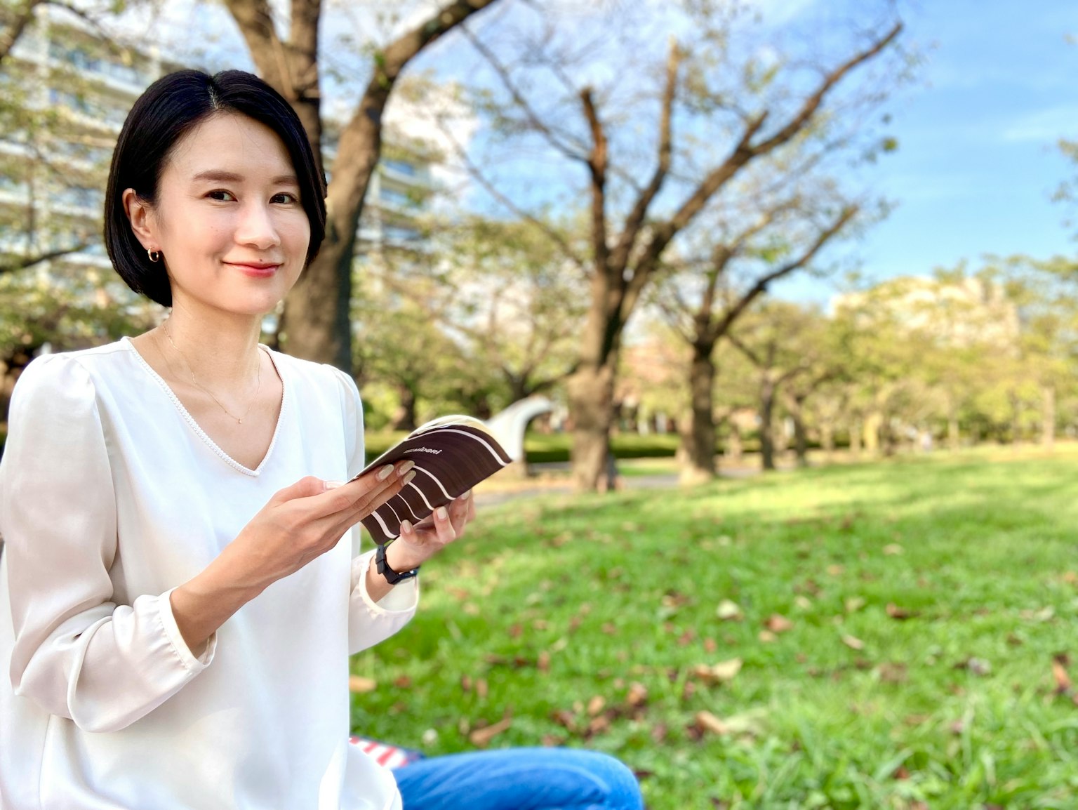 Woman smiling while reading a book in a green park