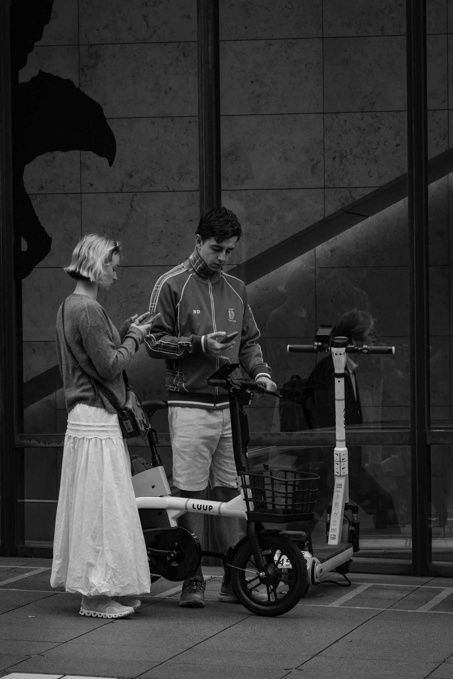A woman in a white skirt and a man in a gray jacket standing by an electric scooter