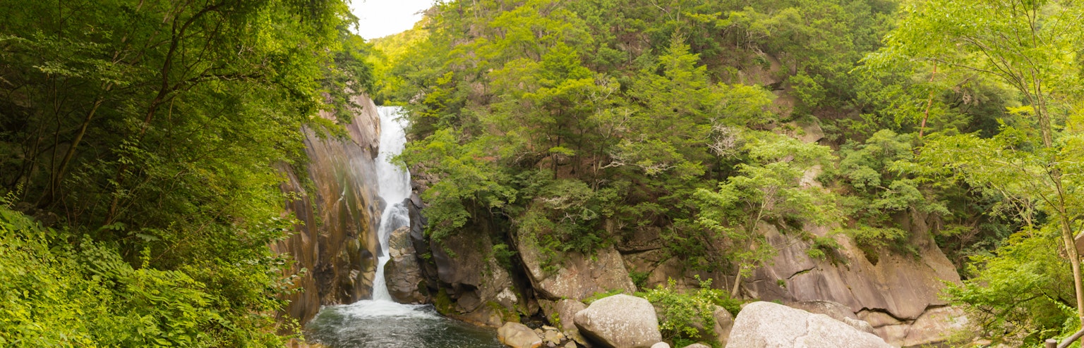 Una cascada que cae entre montañas verdes rodeadas de rocas