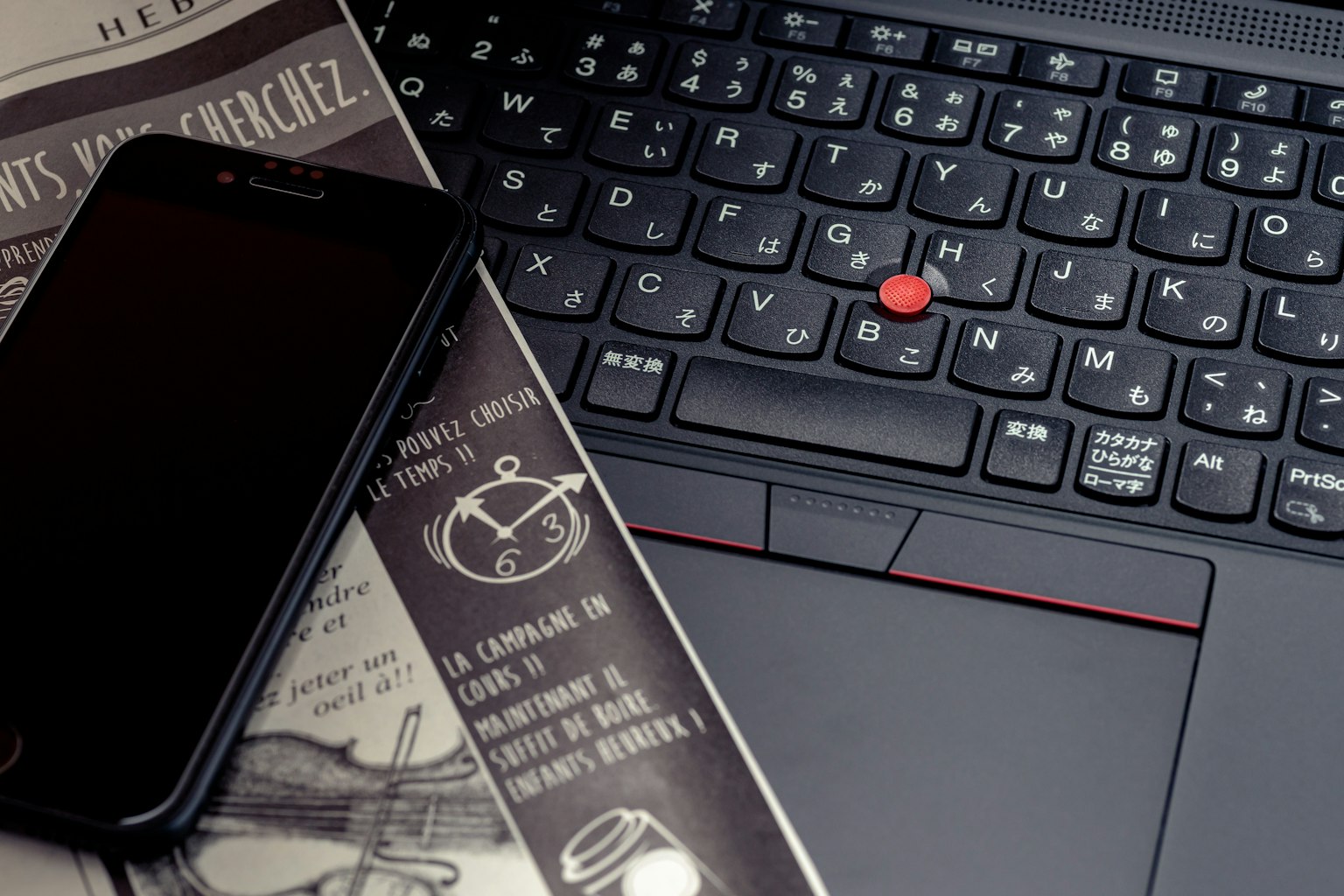 Smartphone nero accanto alla tastiera di un laptop e un giornale
