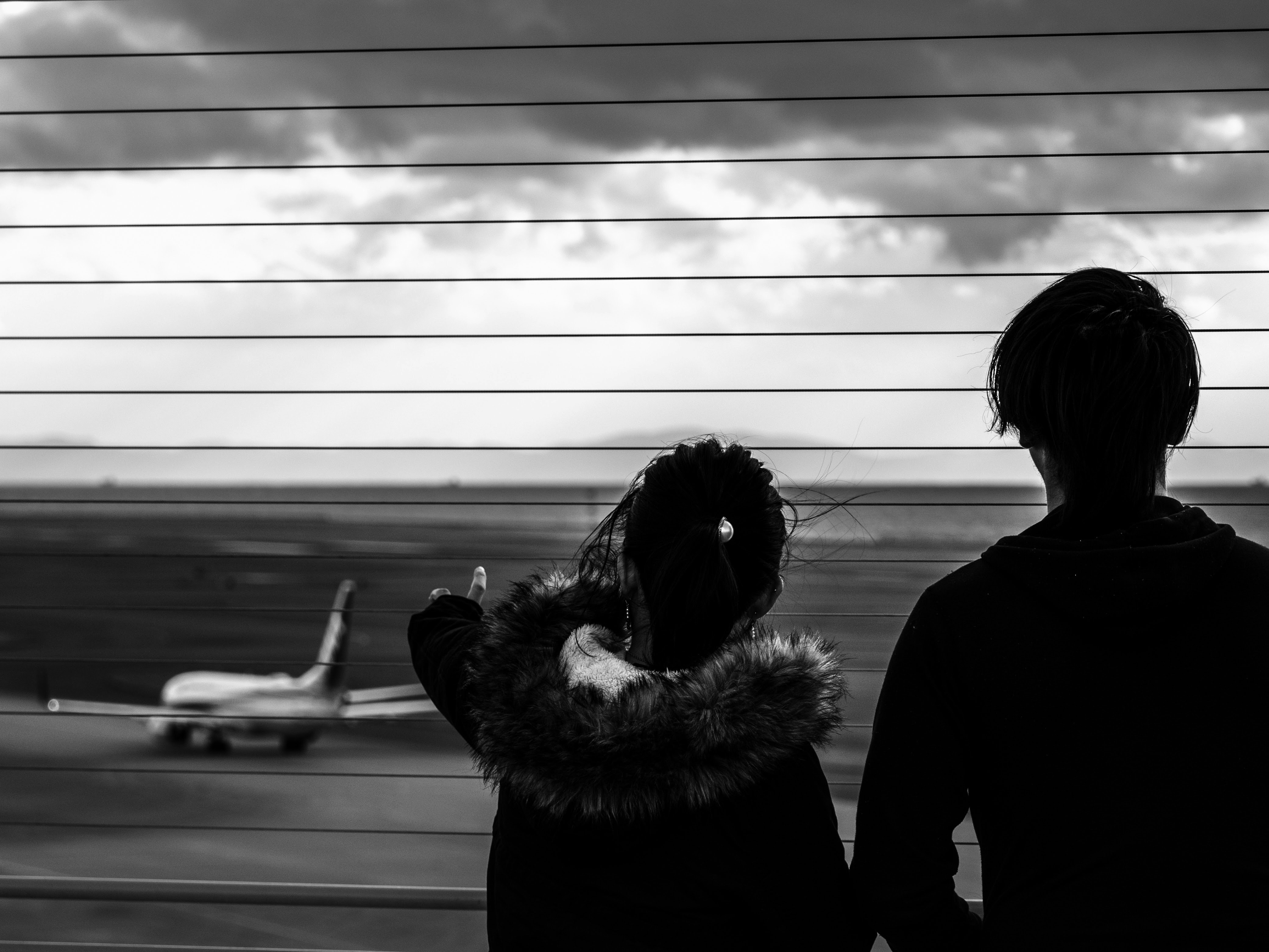 展望デッキから見上げる飛行機とモノクロの二人
