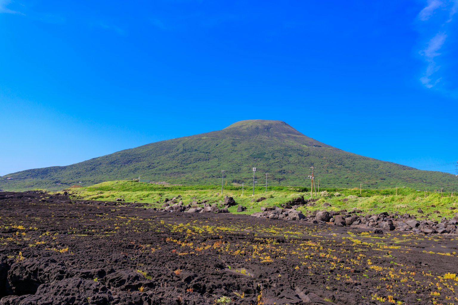 Green mountain under a blue sky with black lava land