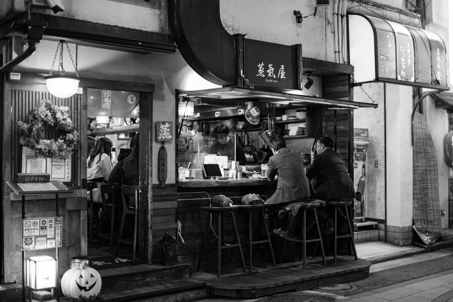 Image en noir et blanc de l'extérieur d'un restaurant avec des personnes assises au comptoir