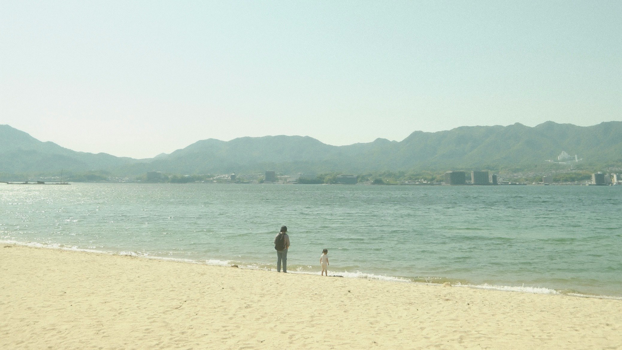 海辺の砂浜を歩く人と遠くの山並み