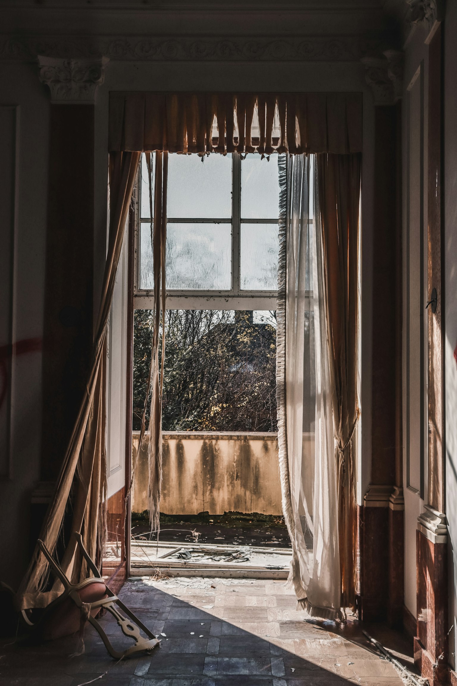 Una vecchia stanza con la luce del sole che filtra da una finestra e tende svolazzanti