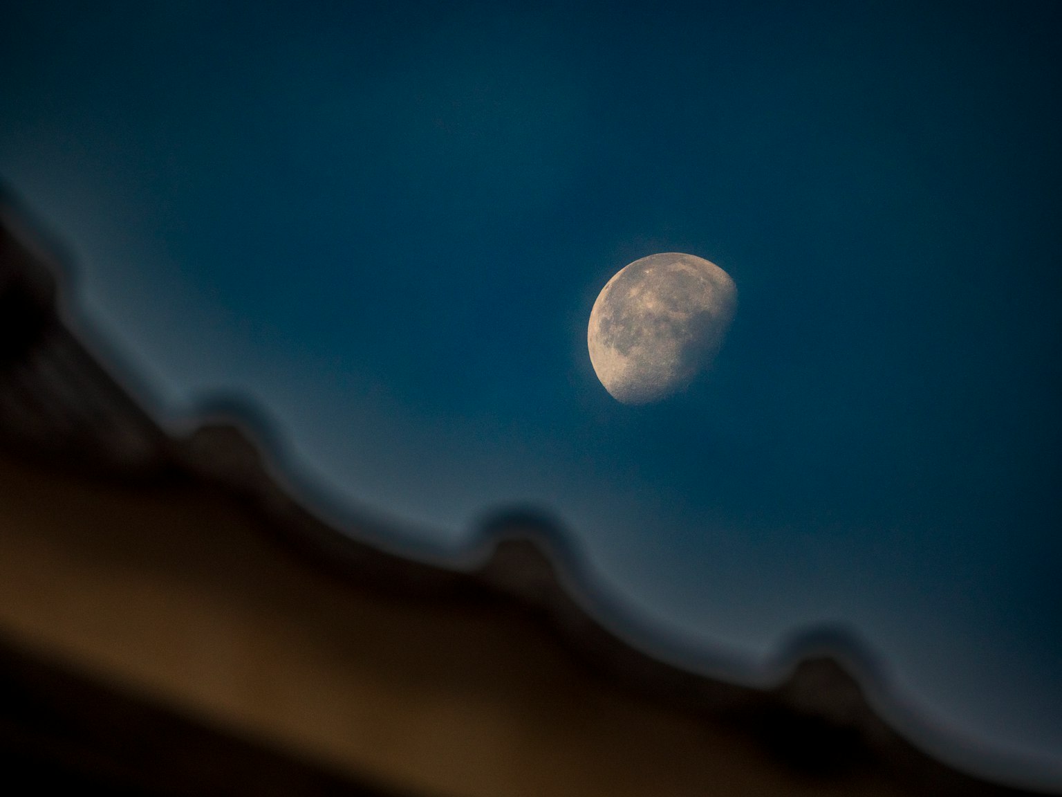 Bulan setengah di langit biru dengan siluet atap