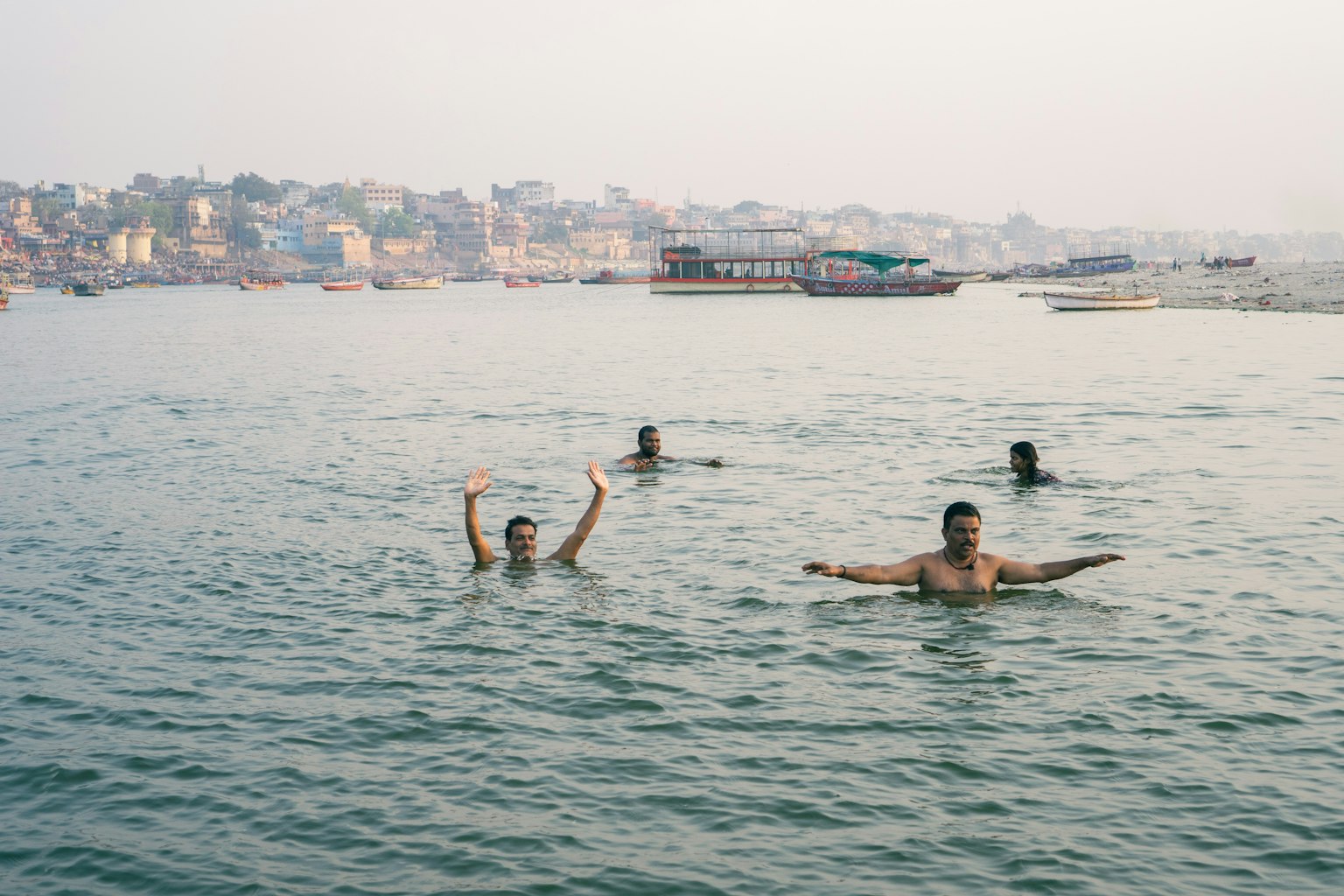 People enjoying the Ganges River with some swimming and cityscape in the background