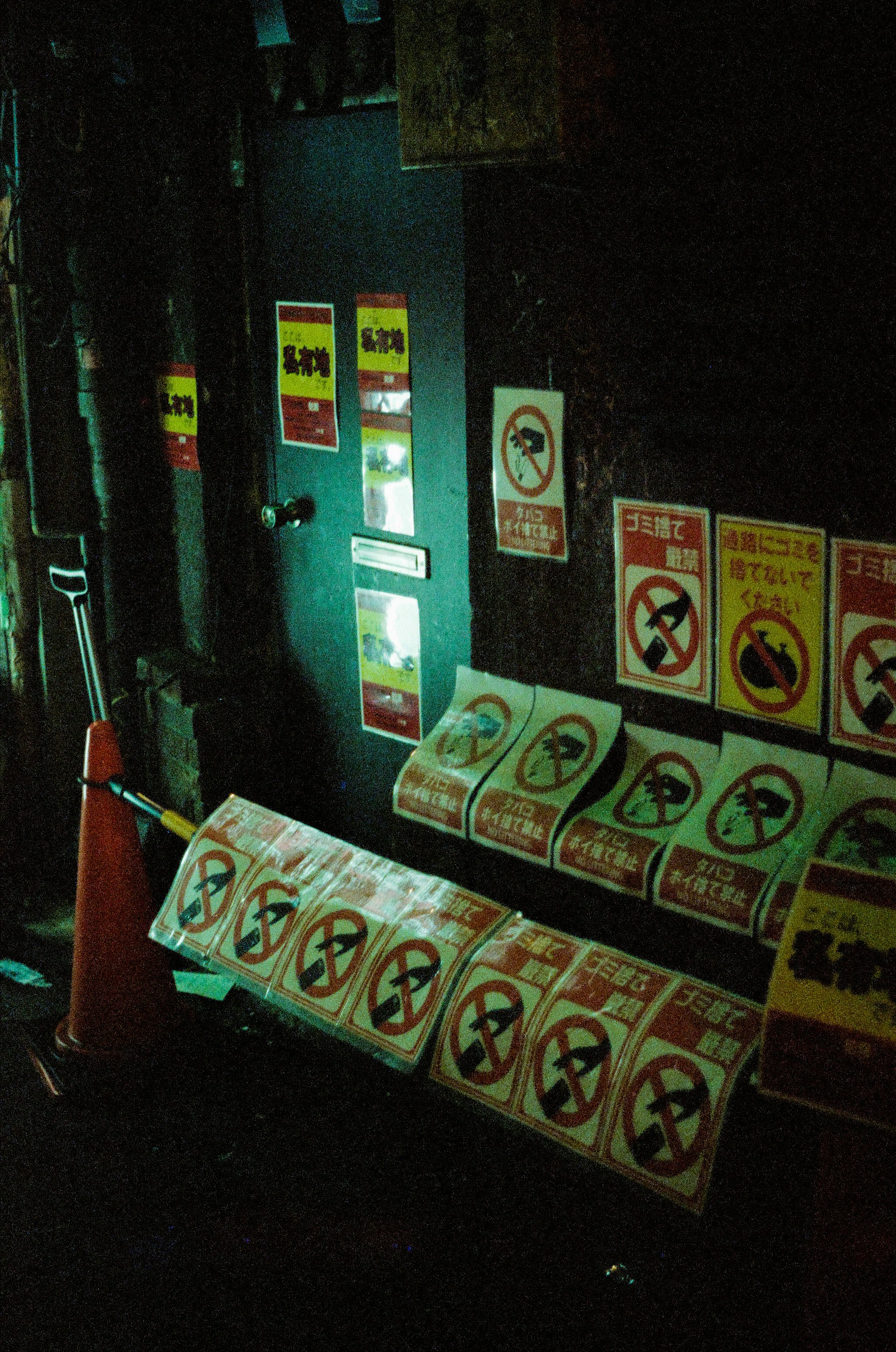 夜の路地に並ぶ掲示ポスターと注意マークのある壁面