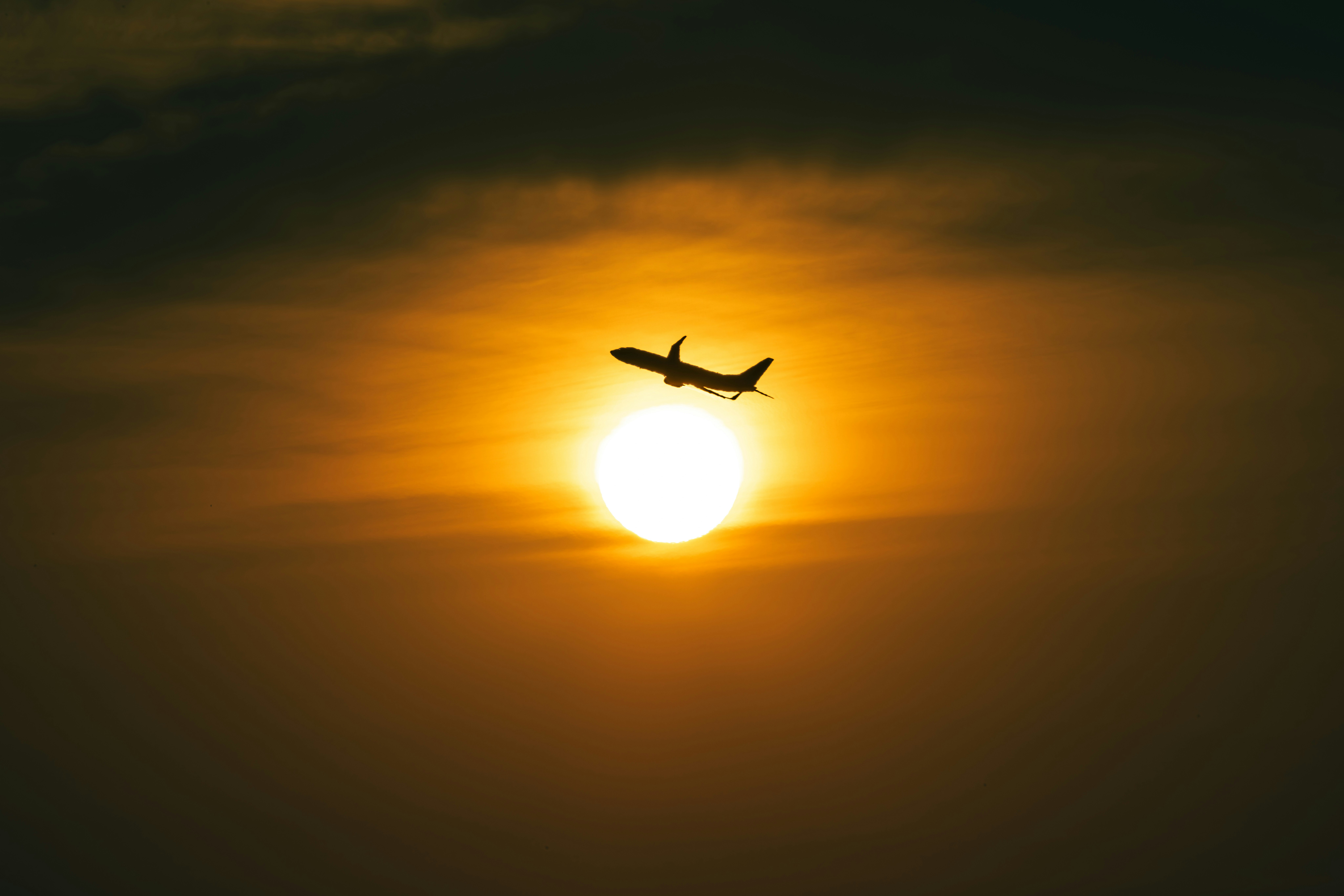 夜明けの太陽の前を飛ぶ飛行機のシルエット