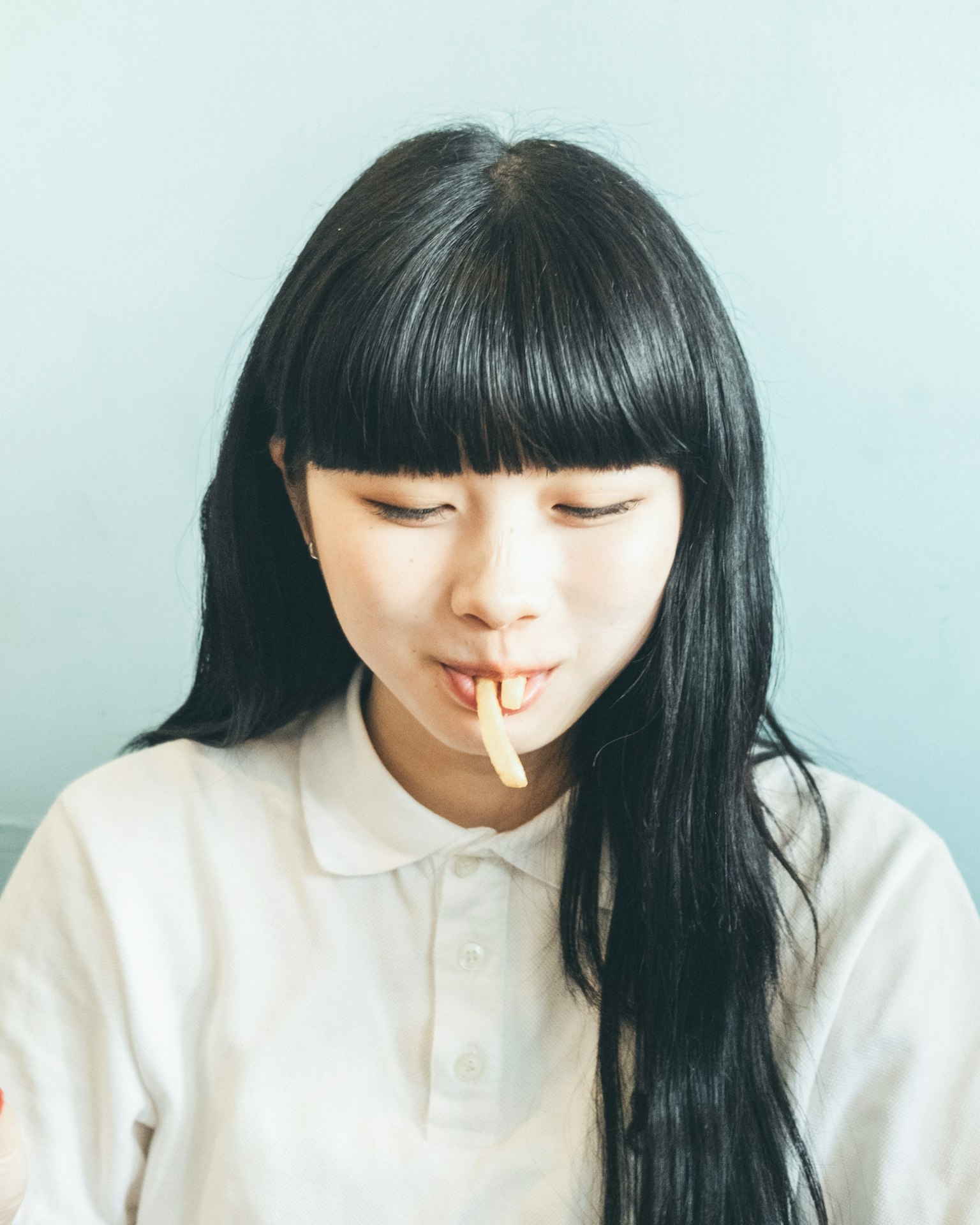 一位長髮黑髮的年輕女性穿著白色襯衫，在藍色背景前微笑