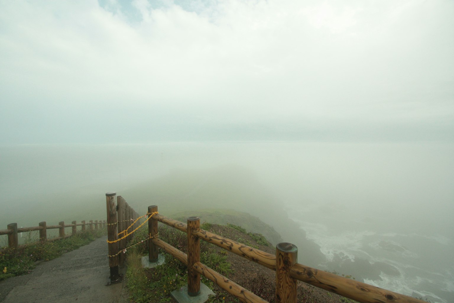 霧氣籠罩的海岸景觀，沿著小路有木欄杆