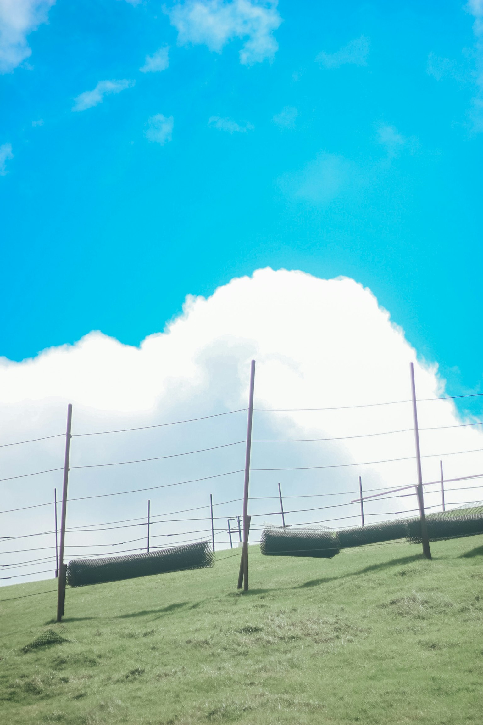 Colina verde con una cerca bajo un cielo azul brillante y nubes