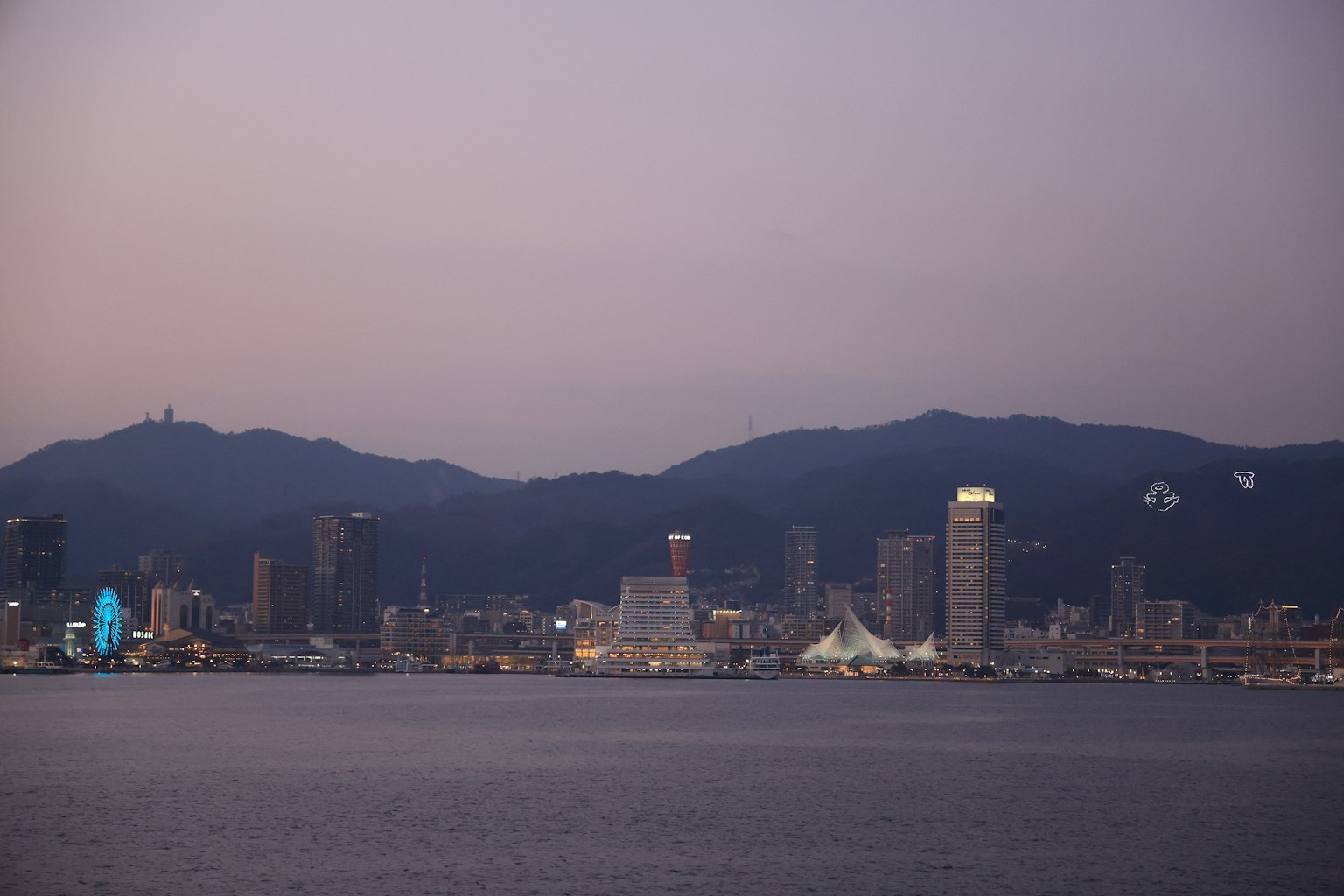 City skyline at dusk with mountains in the background and reflections on the water