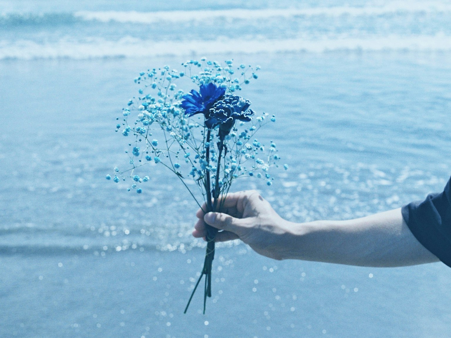 Tangan memegang buket bunga biru dengan latar belakang laut
