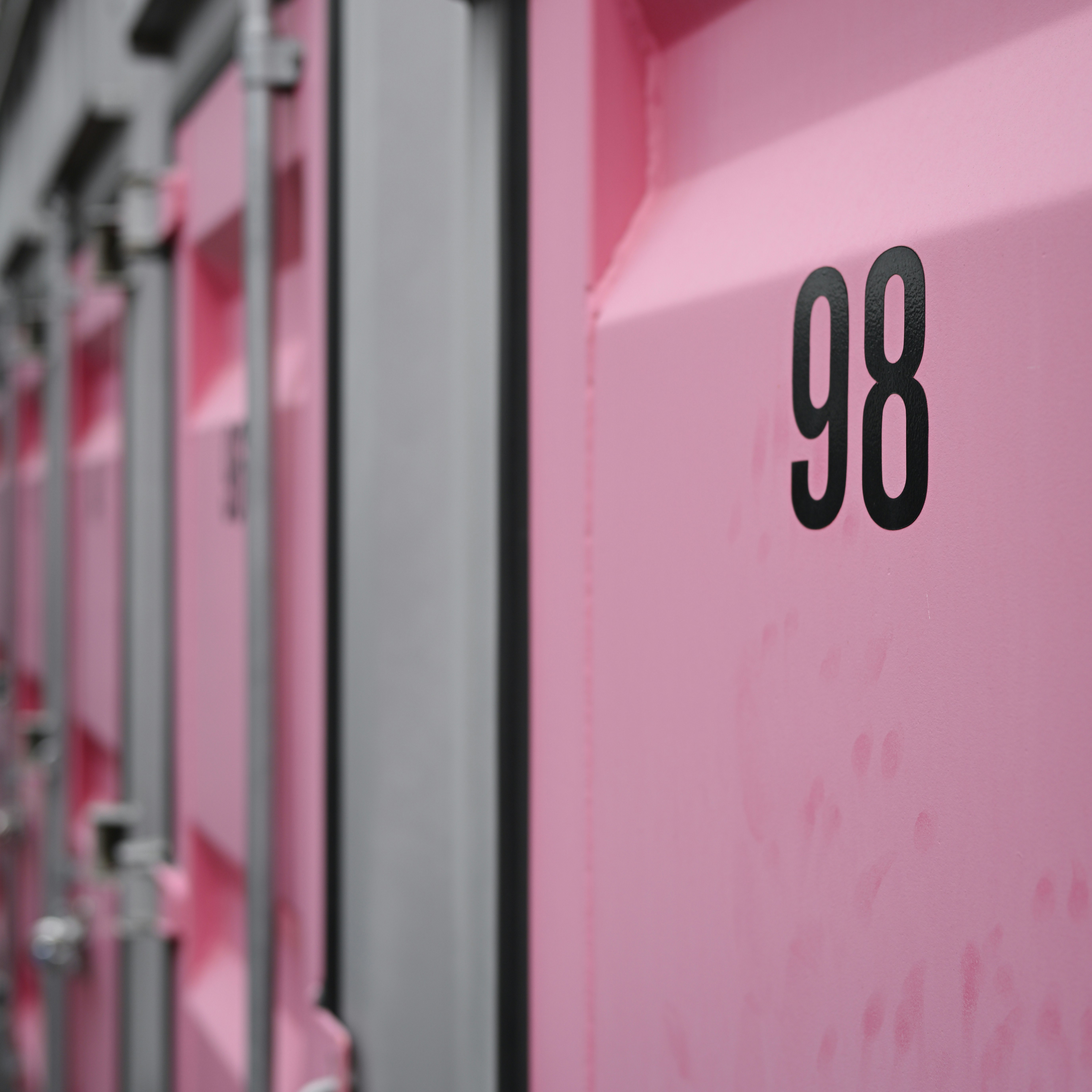 ピンクの倉庫壁に並ぶ「98」看板のある通路