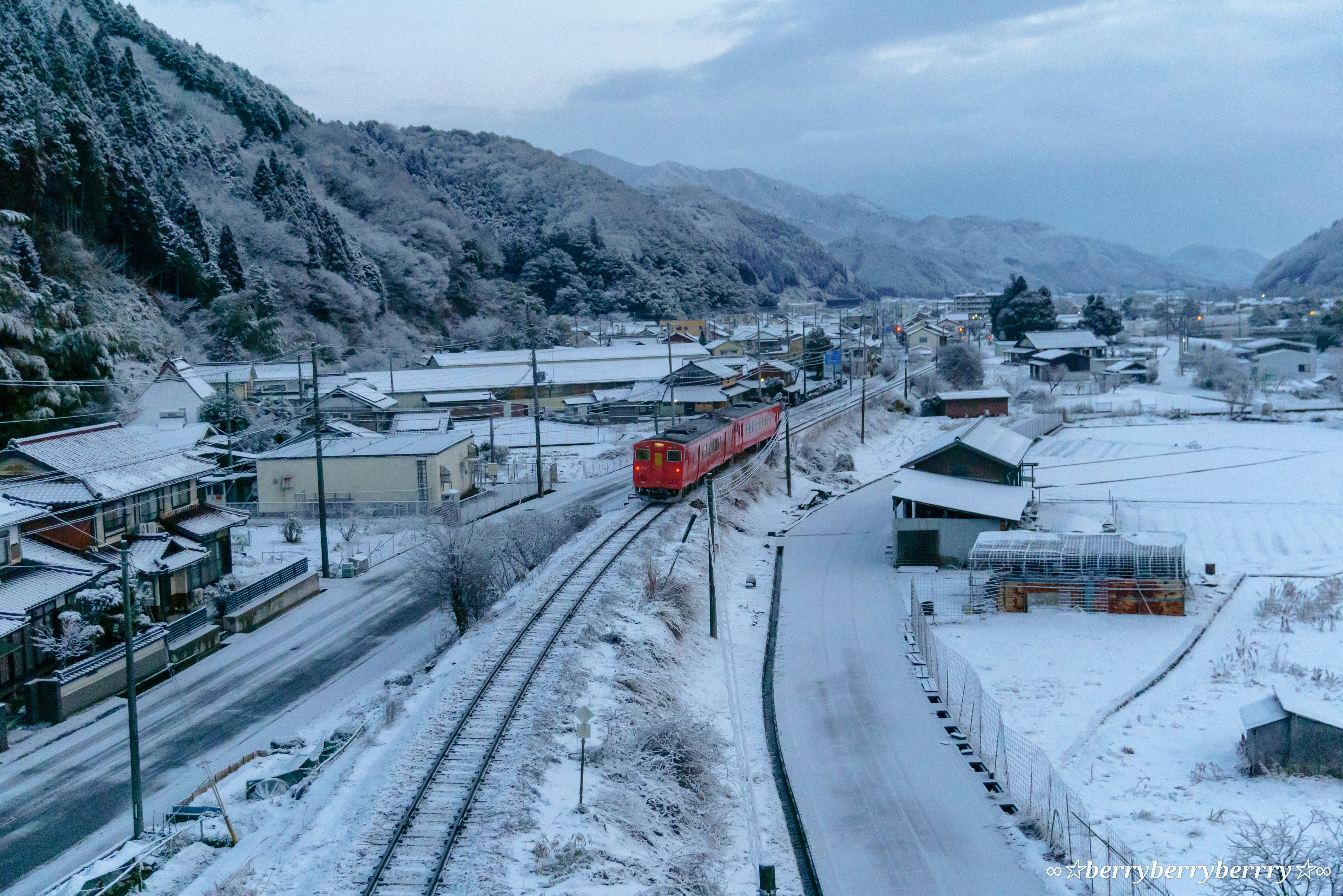 里山を走る雪の鉄道と小さな集落の街並み