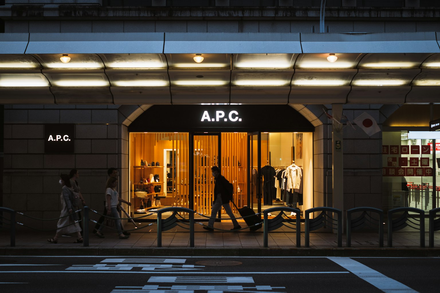 Magasin A.P.C. illuminé la nuit avec des piétons passant