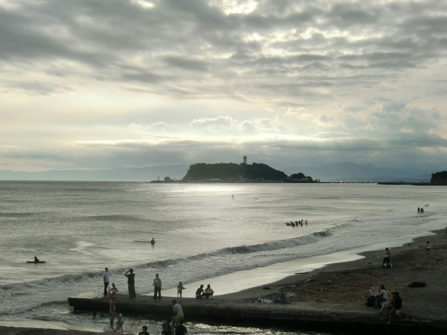 海岸線に沿った人々と遠くの灯台を背景にした静かな海の風景