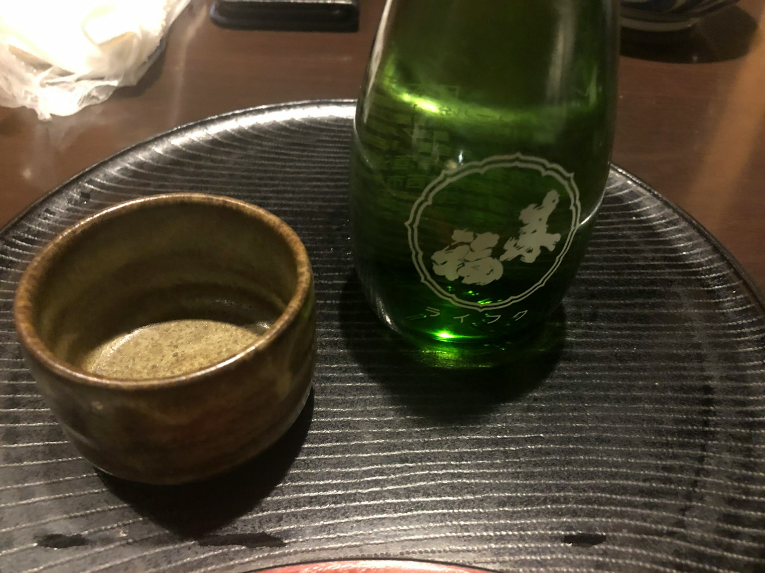 Green bottle and ceramic cup placed on a black plate