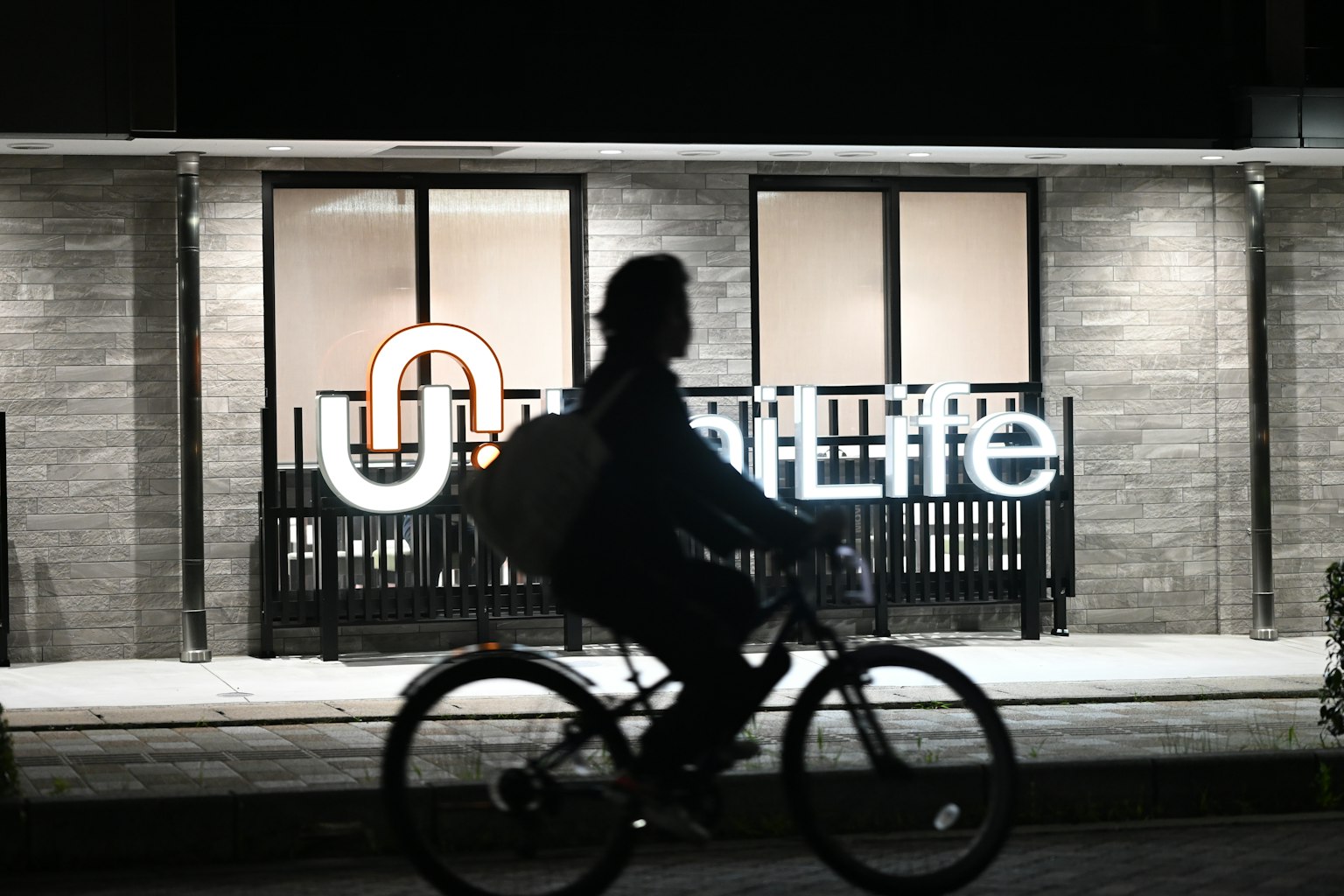 Silhouette di una persona in bicicletta con il logo Life illuminato di notte