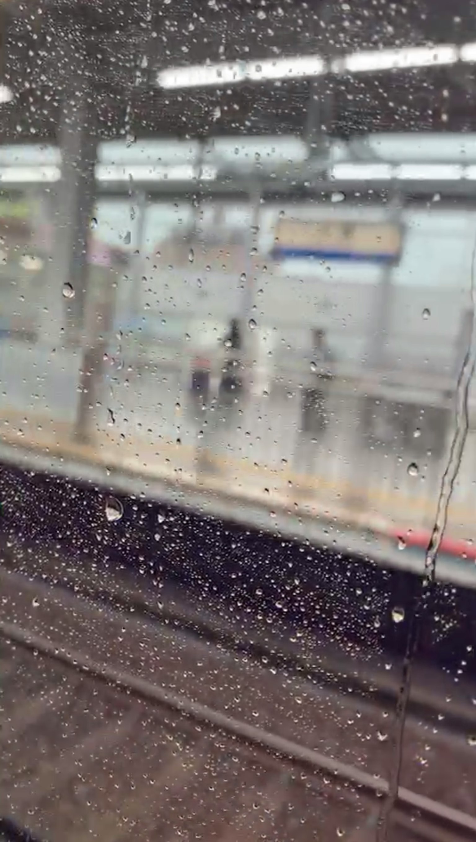 透过雨滴覆盖的窗户看到的火车站和模糊的人影