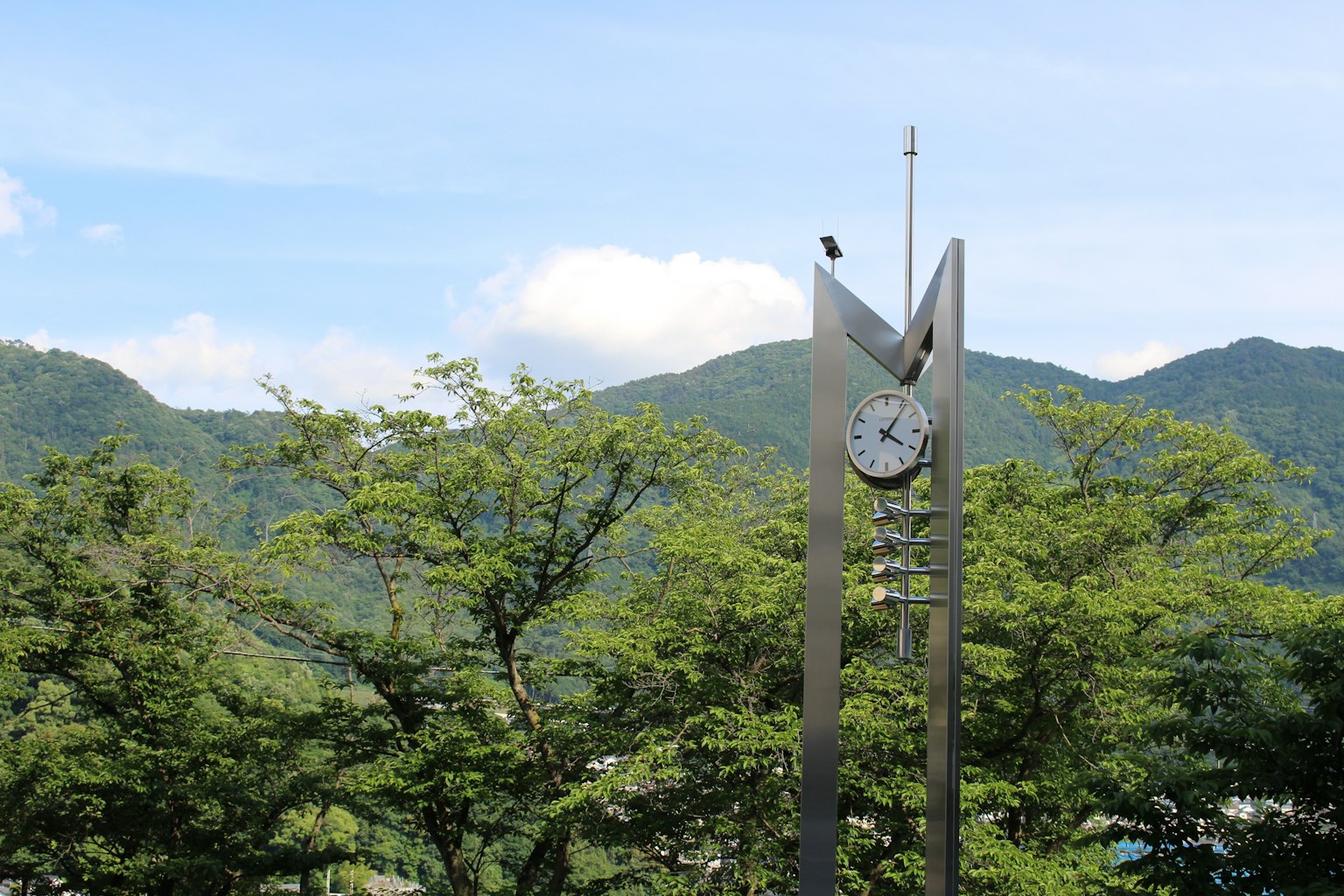 Moderne Uhrturm mit einem Vogel oben umgeben von grünen Bäumen und Bergen