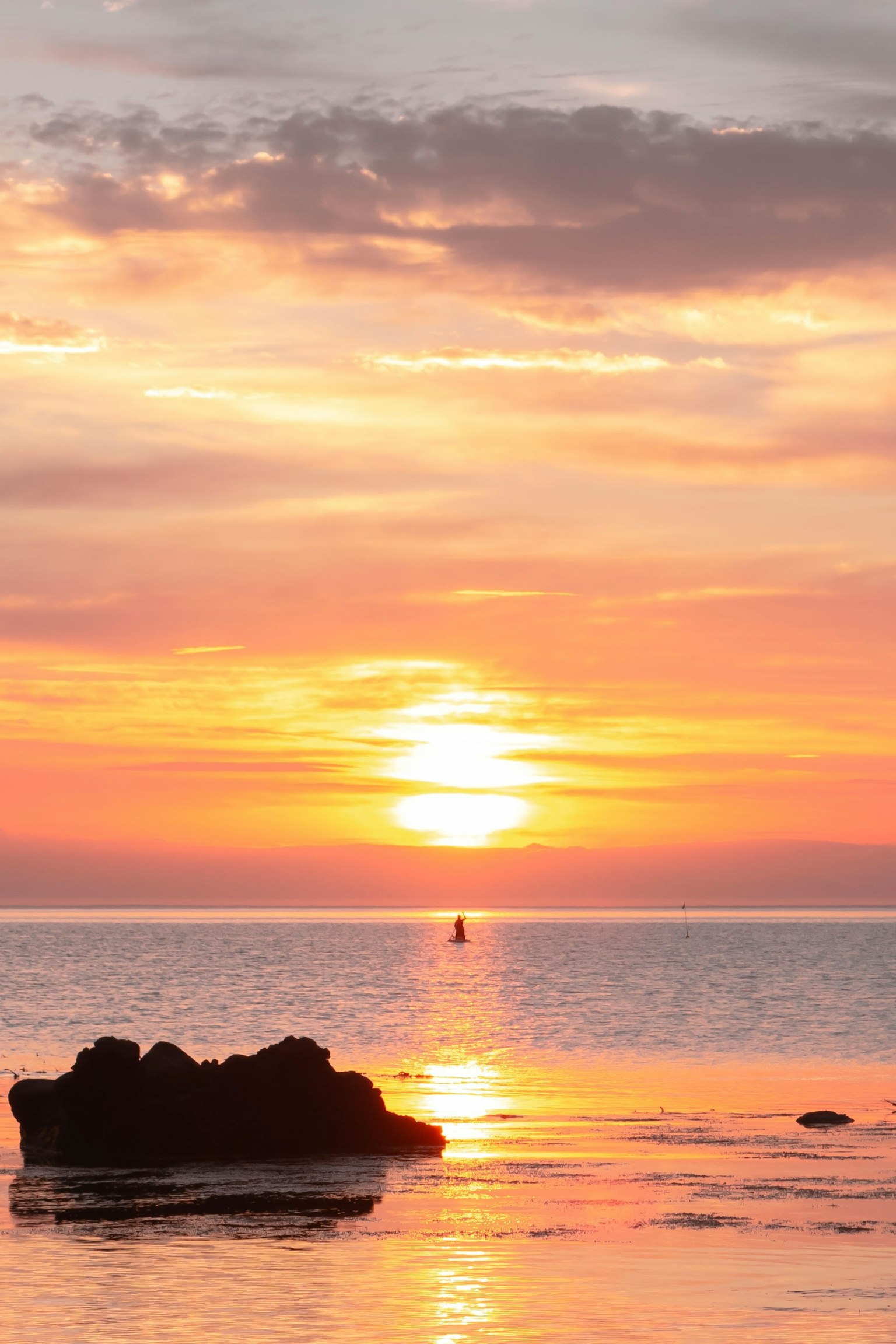 Beautiful sunset reflecting on the sea with a rock on the shore and calm waters