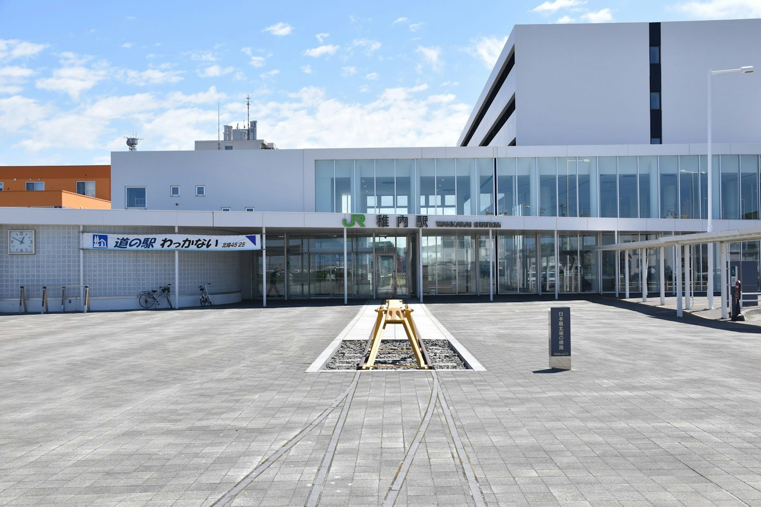 Modern building entrance with wide paved plaza under blue sky and clouds