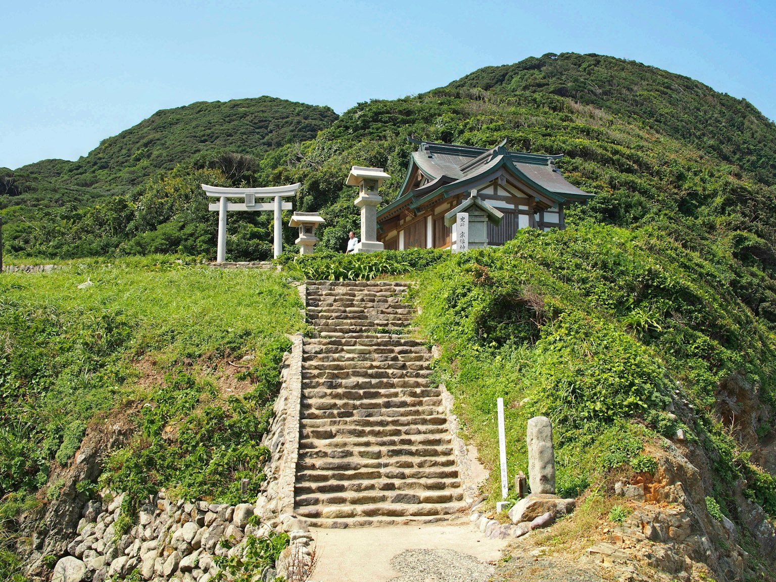 Pemandangan indah sebuah kuil dengan tangga dan gerbang torii di atas bukit hijau