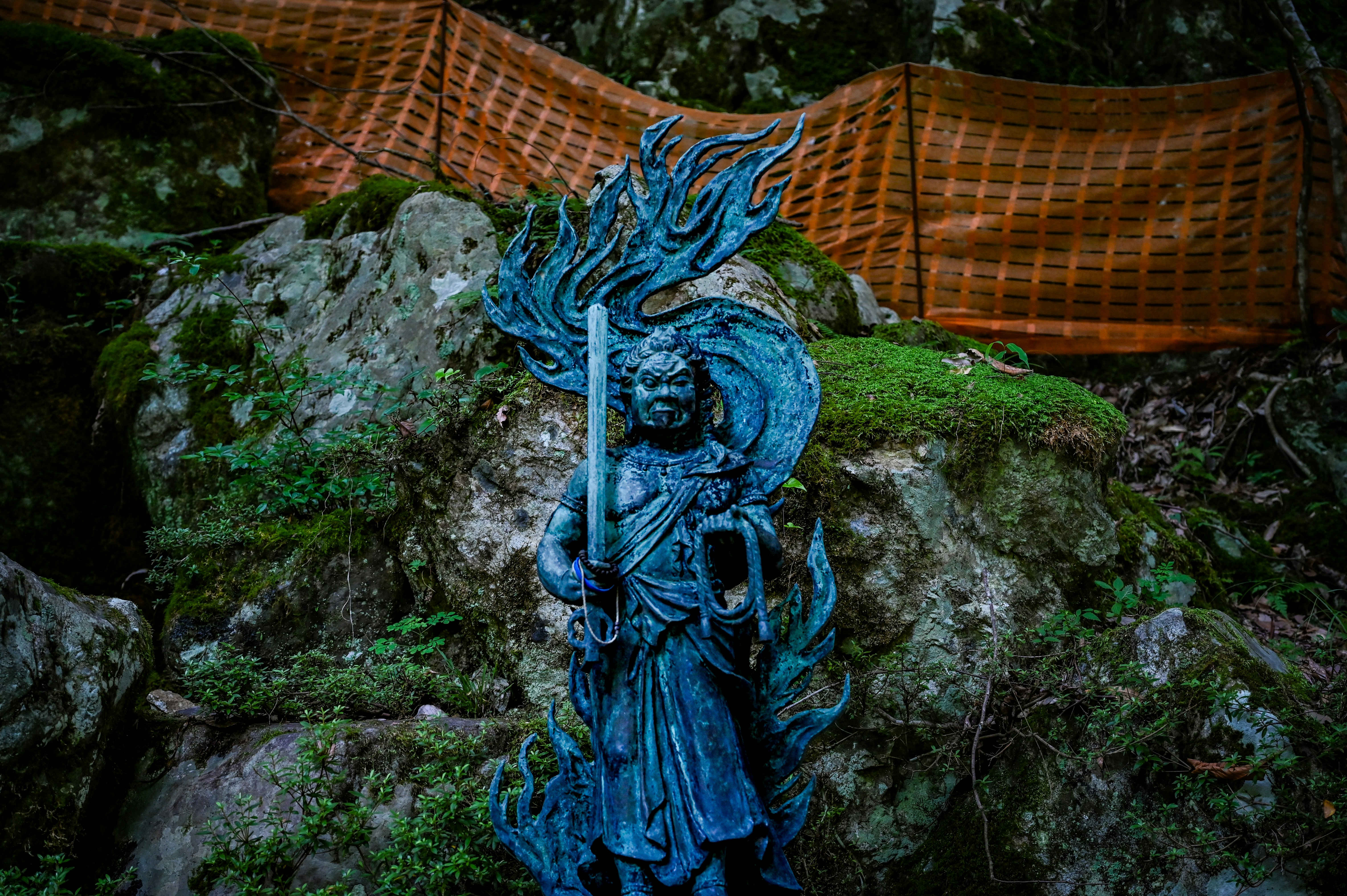 長滿青苔的岩石上擺放的藍色神像與編織籃子，花園場景