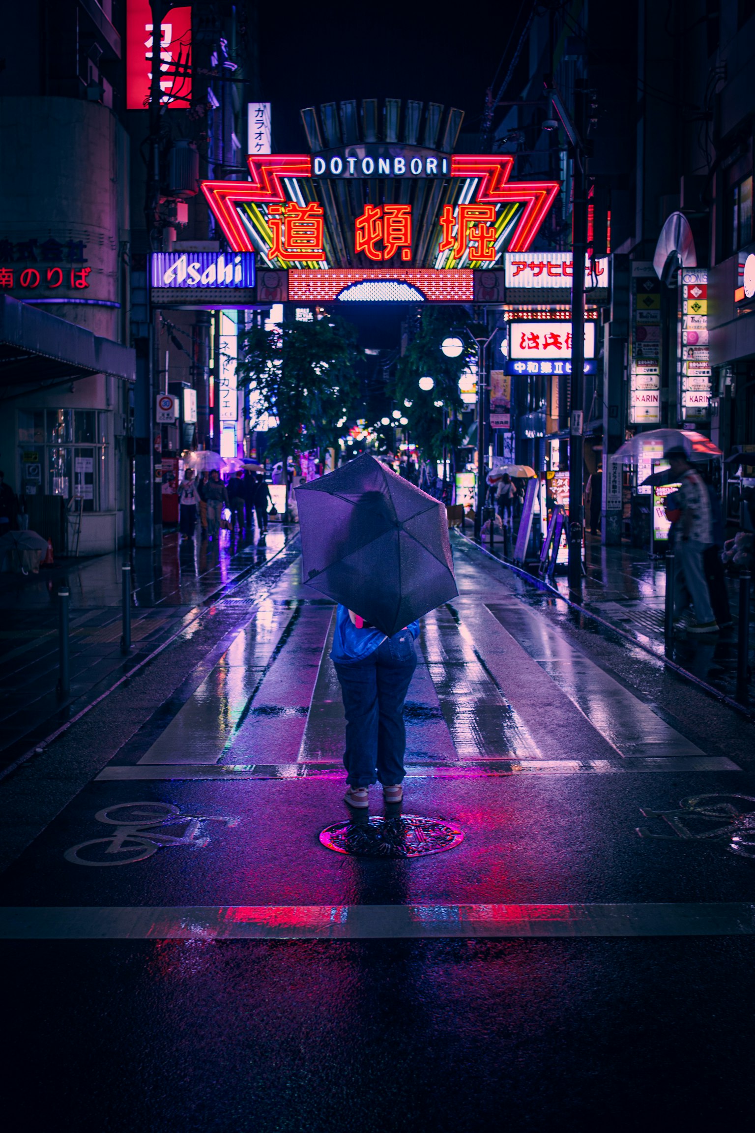 Une personne tenant un parapluie se tient sous la pluie devant des enseignes au néon dans une rue de la ville