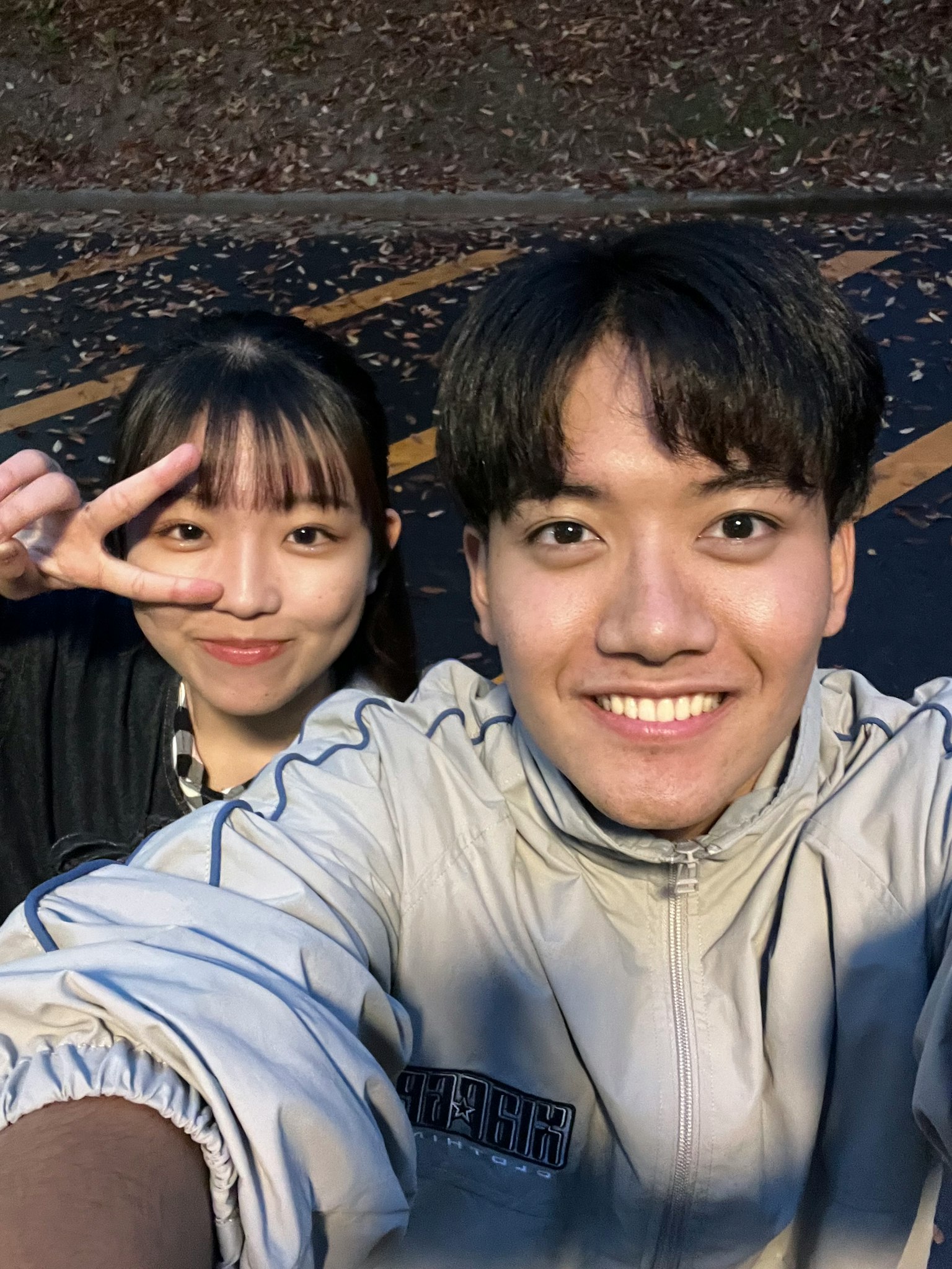 Un selfie di due giovani in un parco sorridenti con un uomo che sorride e una donna che fa il segno della pace