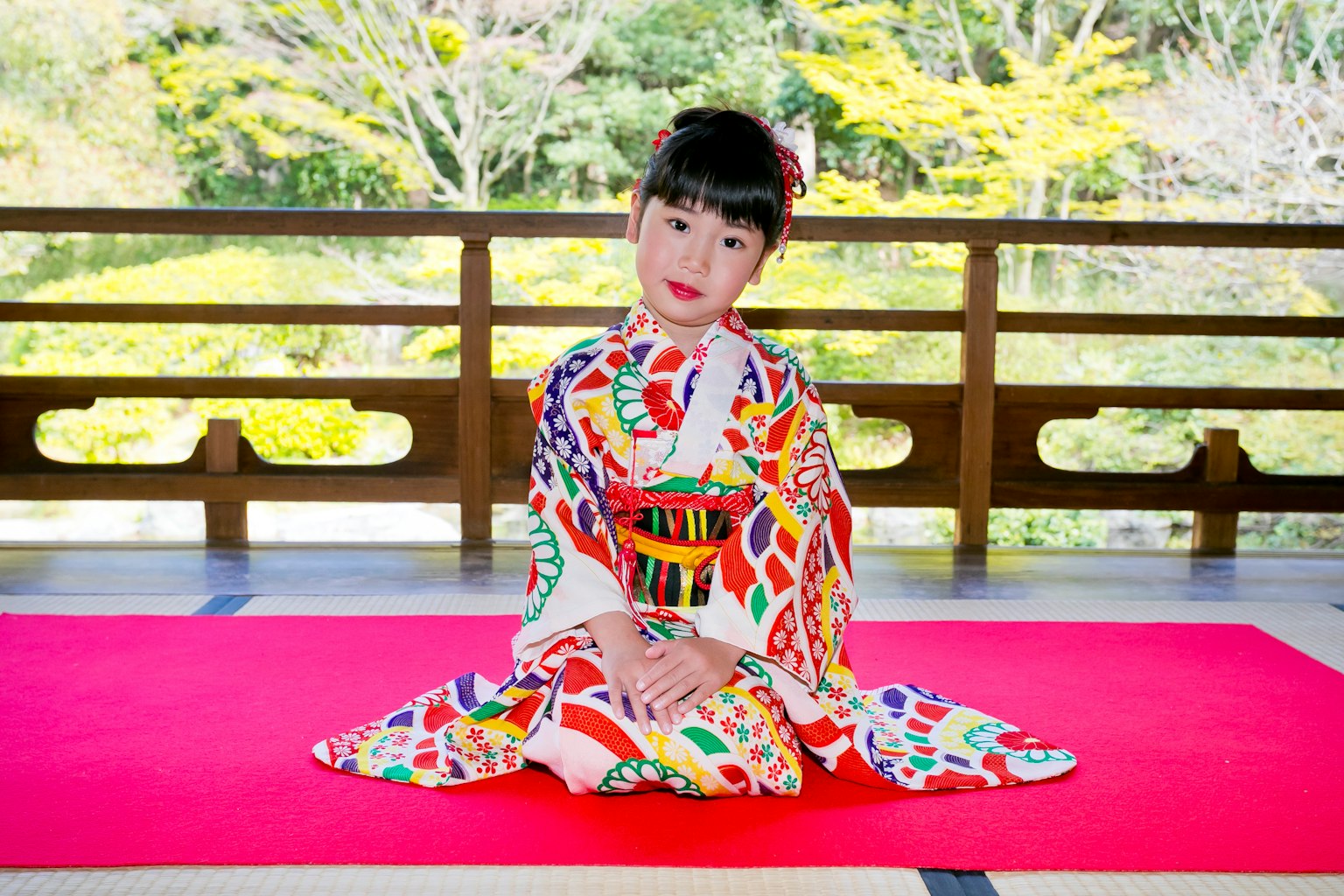 Un bambino vestito con un kimono colorato seduto su un tappeto rosso
