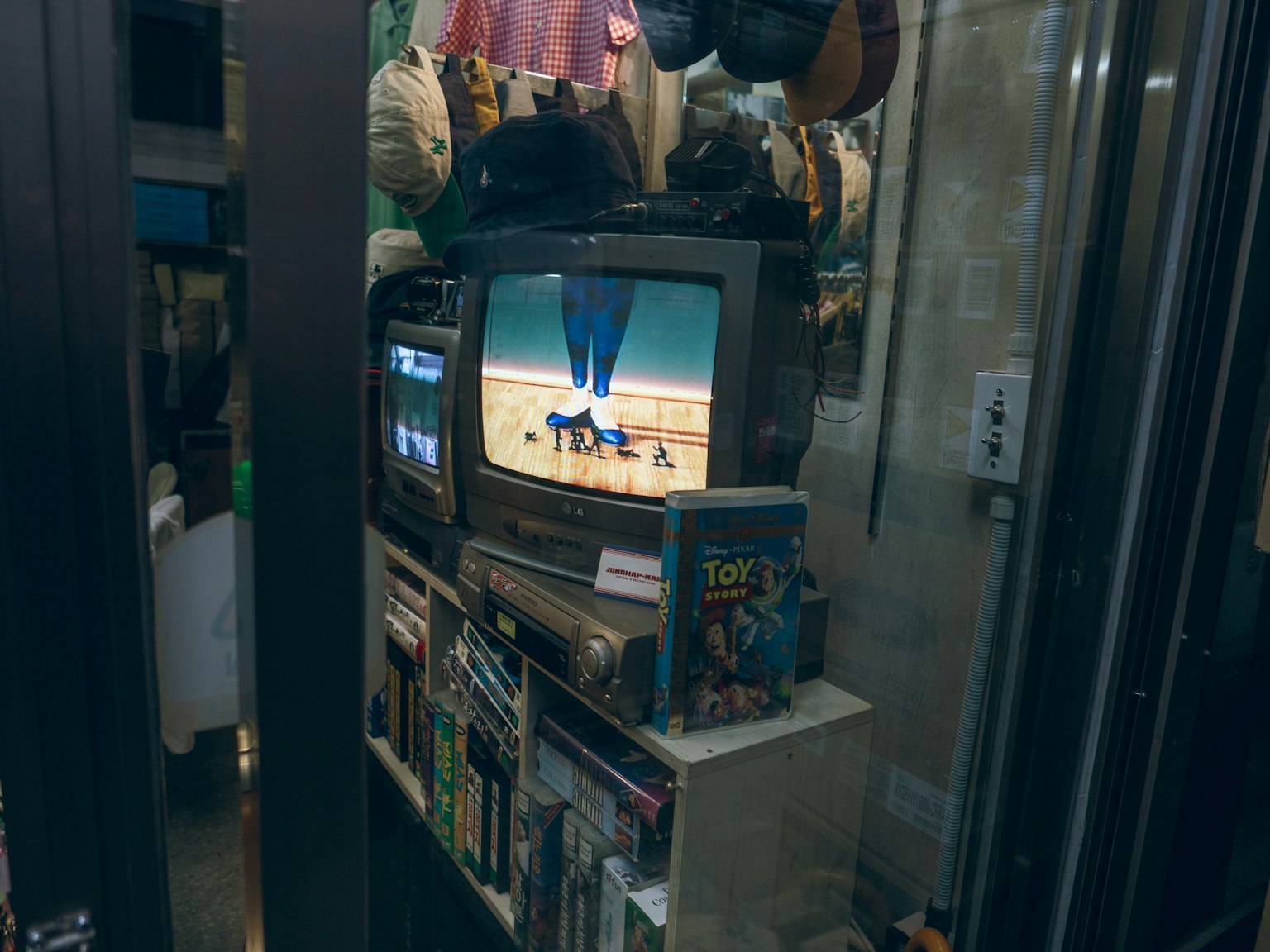 Sebuah televisi vintage menampilkan gambar dikelilingi berbagai barang eklektik di sudut toko