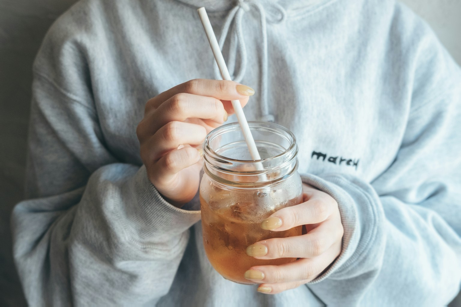 Person in gray hoodie sipping a drink through a straw