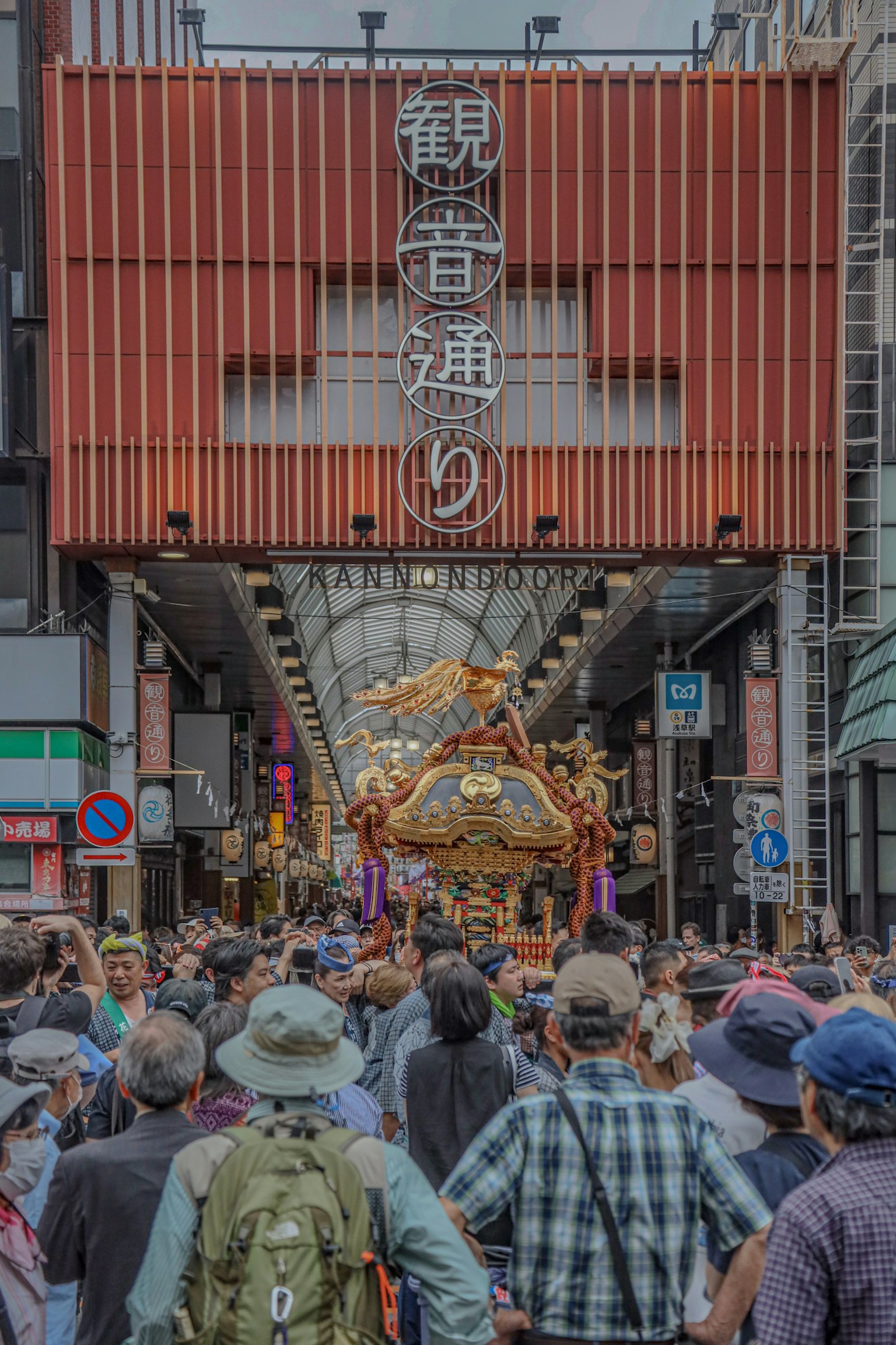 Folla riunita in una strada affollata con un santuario portatile che si muove sotto un'insegna di centro commerciale
