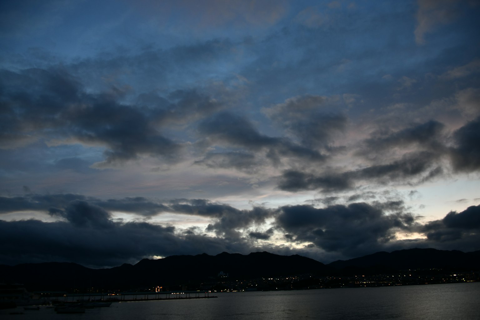 Ein dunkler Himmel mit Wolken über einer Küste mit fernen Lichtern