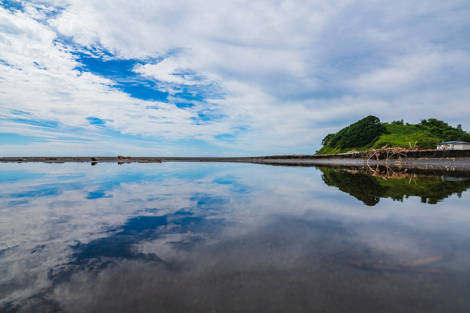Ruhiges Wasser, das Wolken und einen grünen Hügel spiegelt