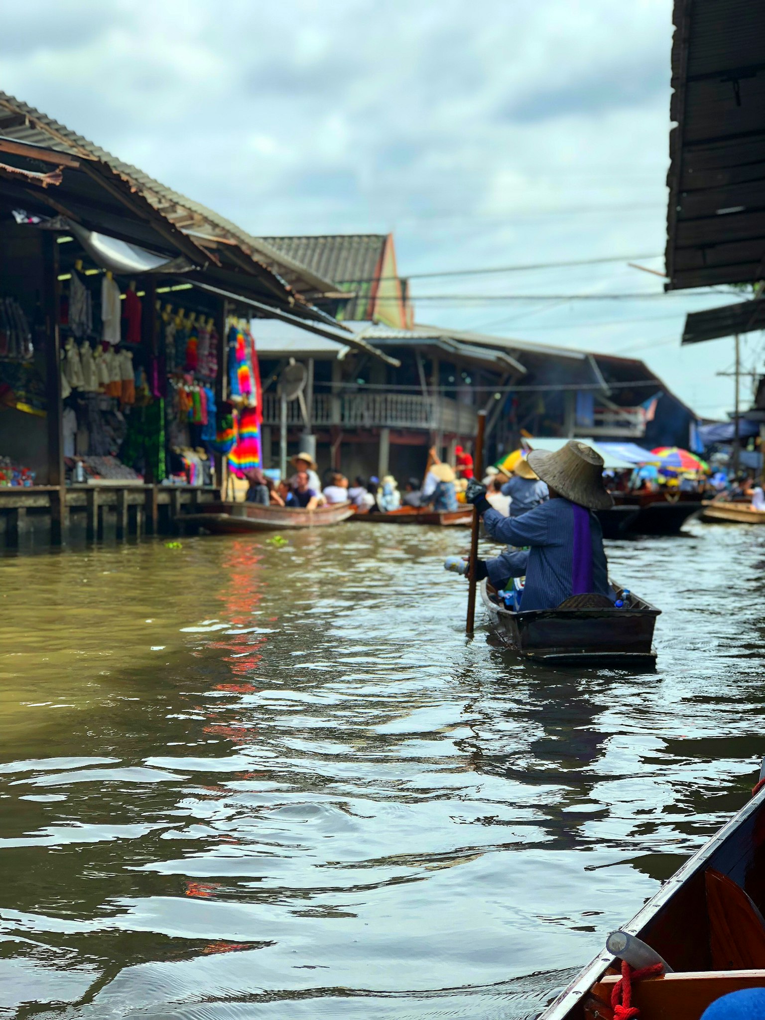 Foto seseorang di perahu di pasar terapung dengan kios di sepanjang air