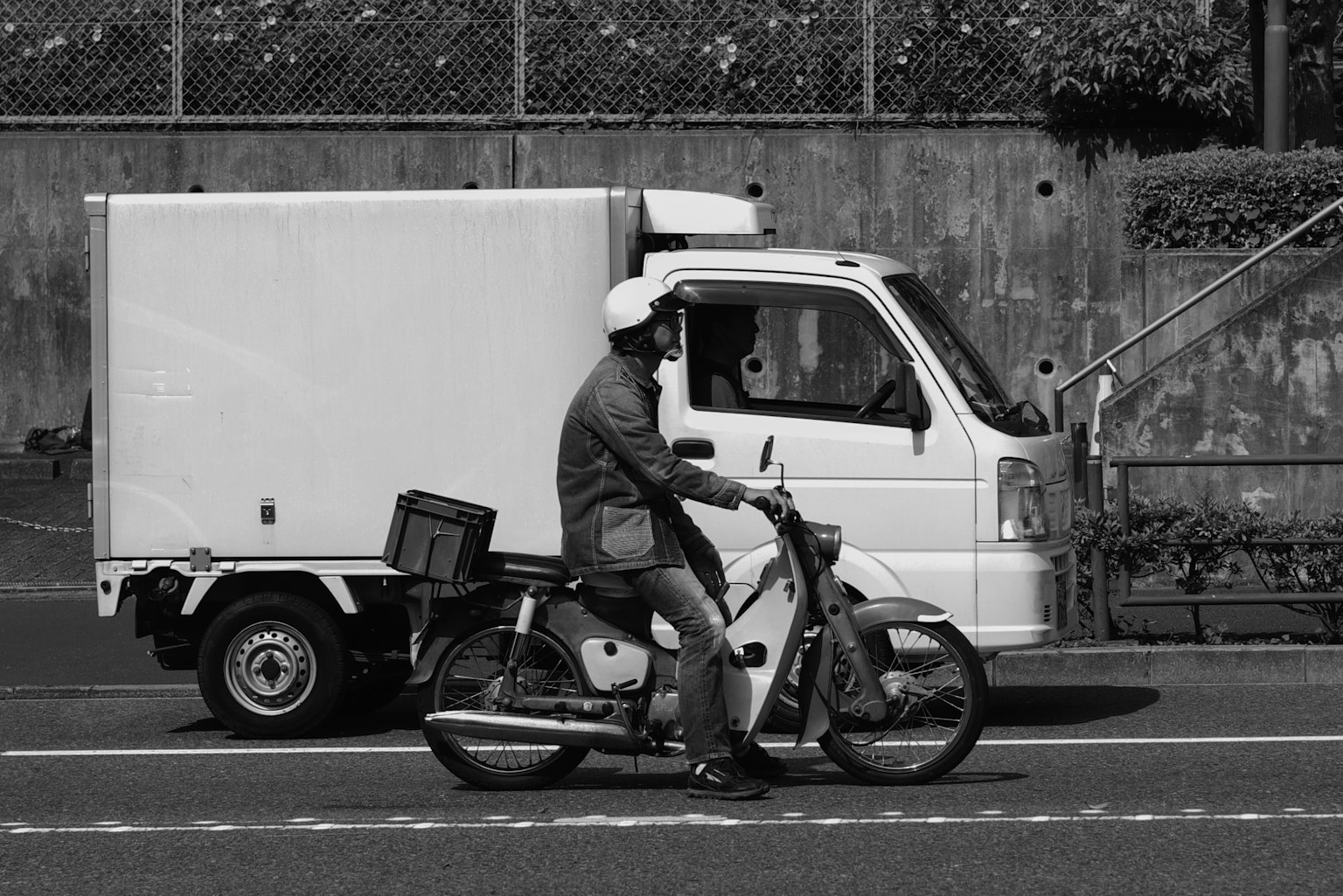 Ein Mann auf einem Motorrad neben einem weißen Lastwagen in einer schwarz-weißen städtischen Umgebung