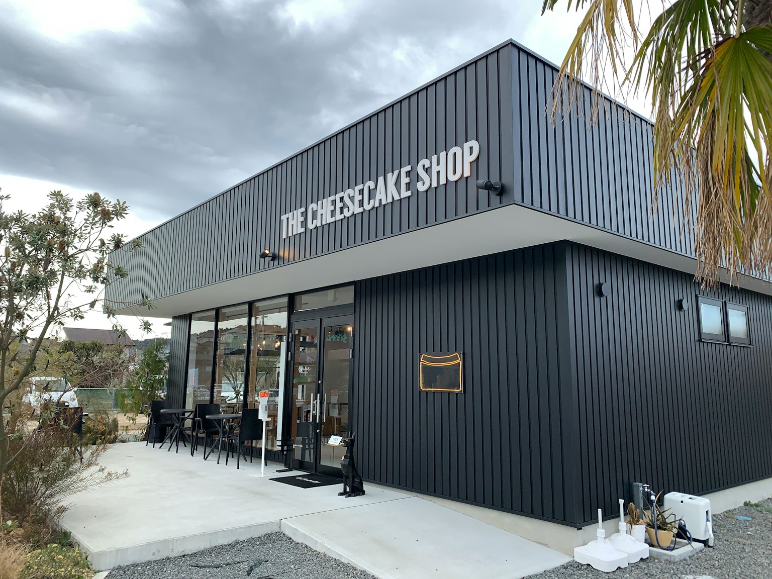Modern exterior of The Cheesecake Shop featuring black metal cladding and large windows