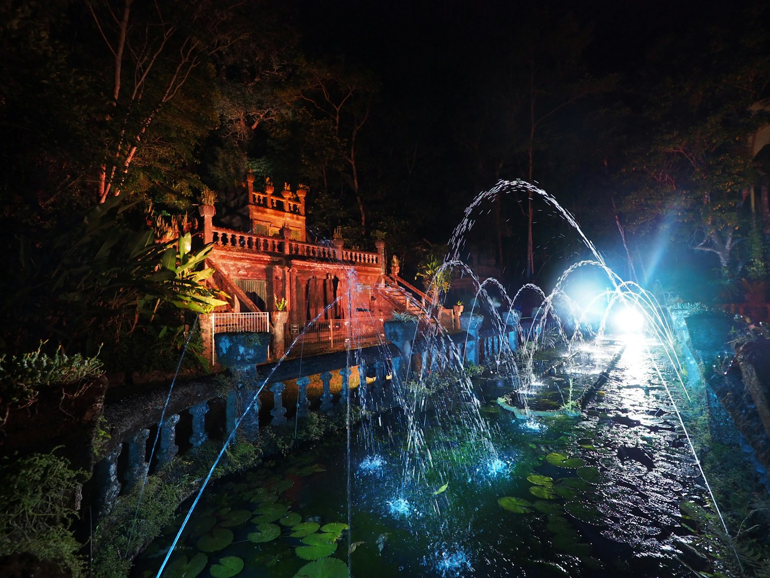 Schöner Brunnen und altes Gebäude in einem Garten bei Nacht
